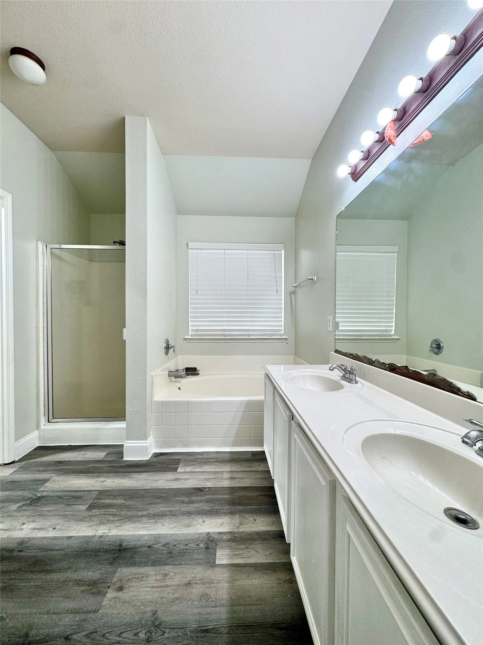 Wood-finish flooring with a dual-sink vanity, built-in bathtub, and separate shower enclosure