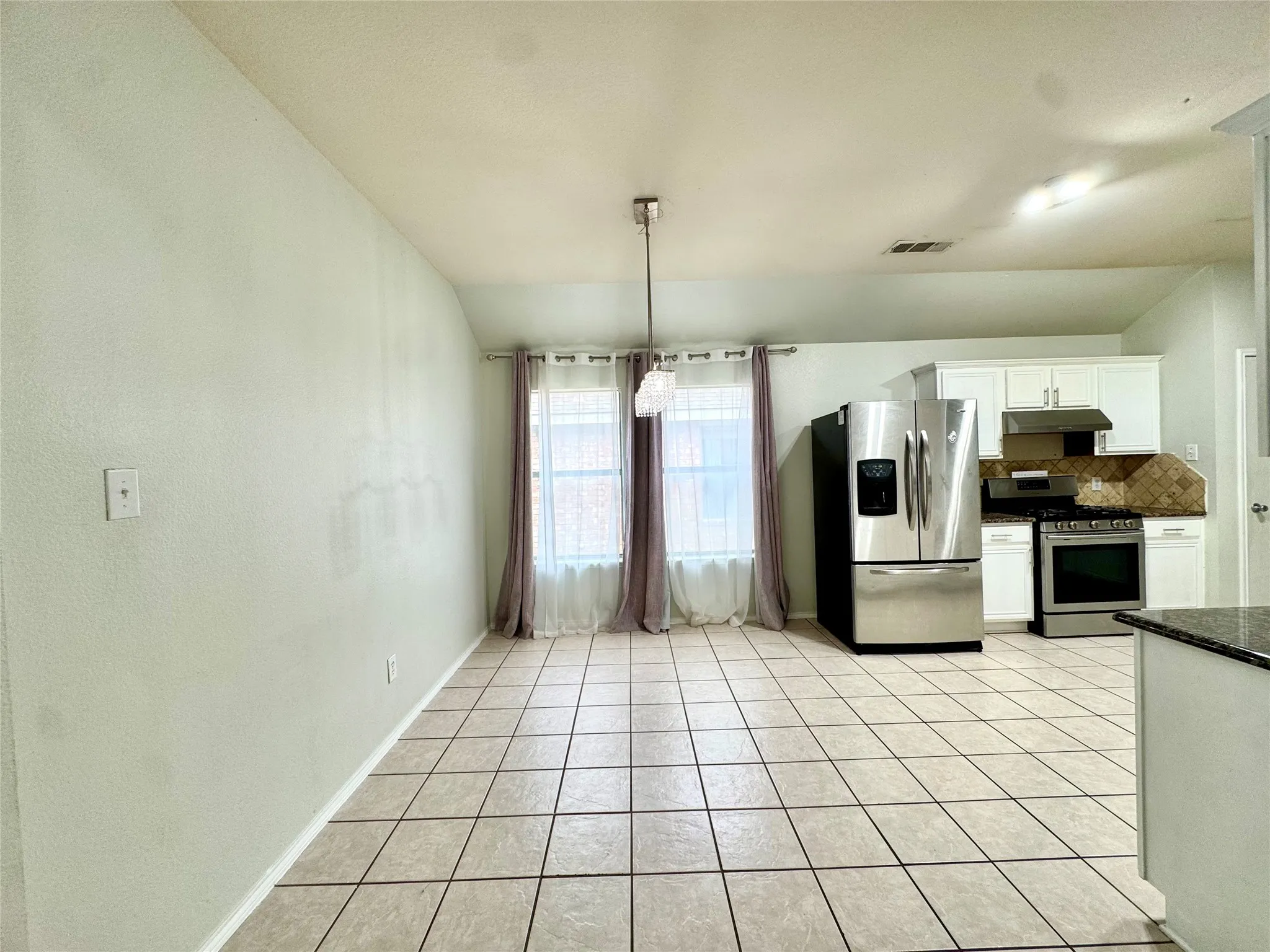 Tile flooring throughout, white upper cabinetry, stainless steel refrigerator, stainless steel range, and a tiled backsplash