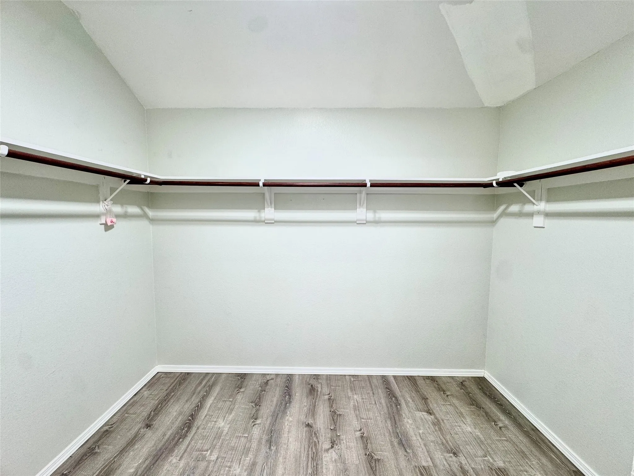 Wall-mounted shelving system with hanging rods, white painted walls, and wood-finish flooring
