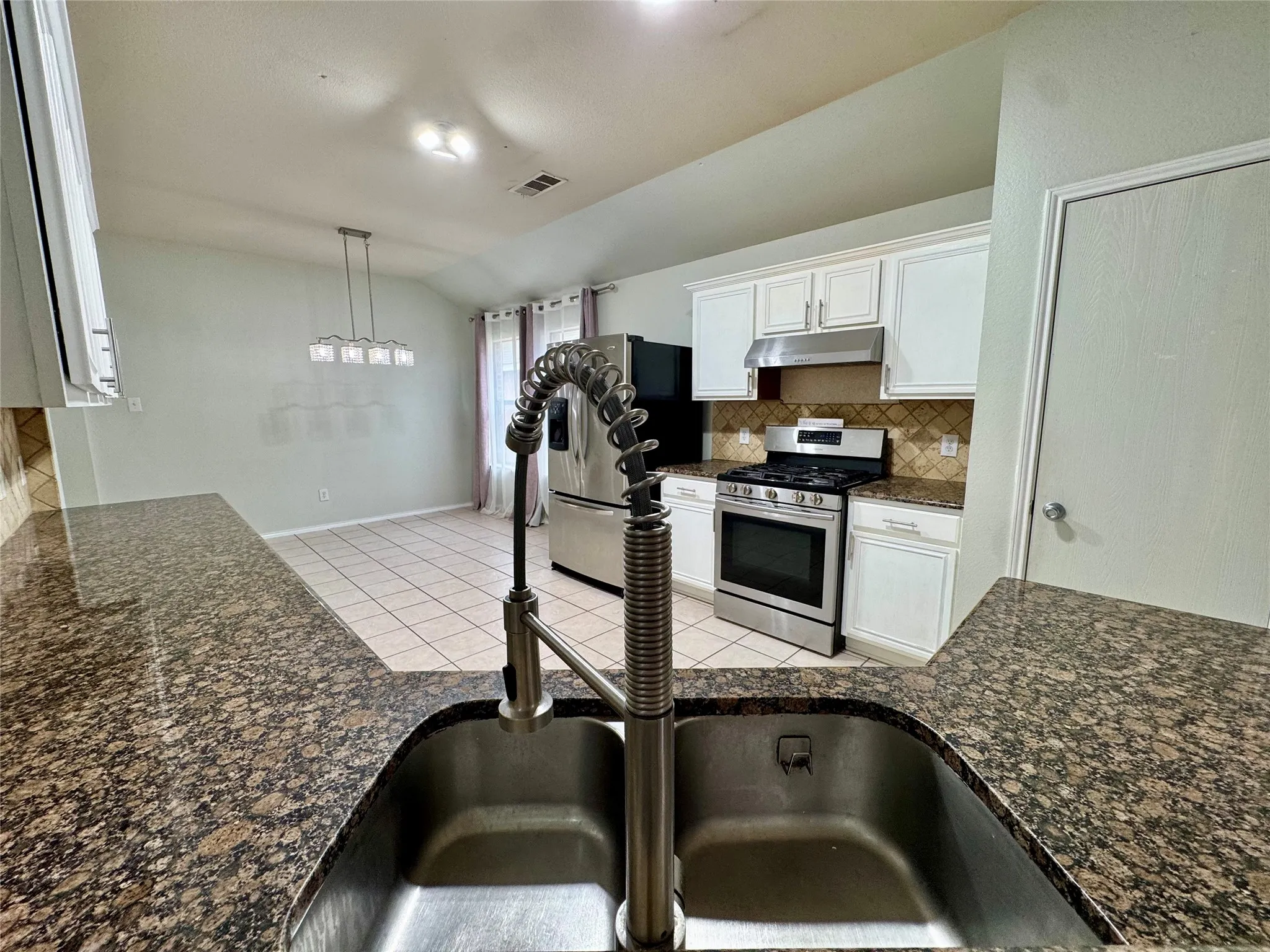Kitchen with stone countertops, stainless steel appliances, white cabinetry, and tile backsplash