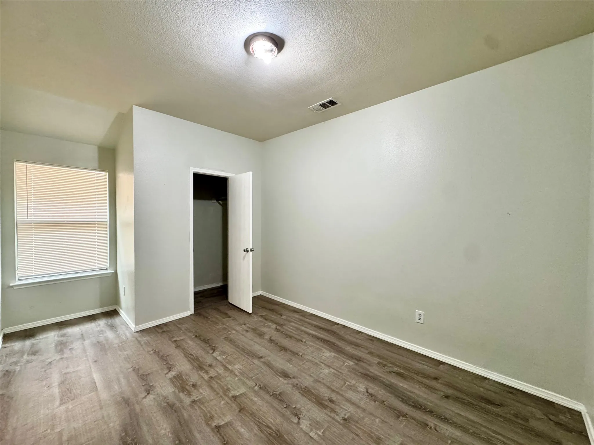 Wood-finish flooring throughout, bright walls, and a window with blinds