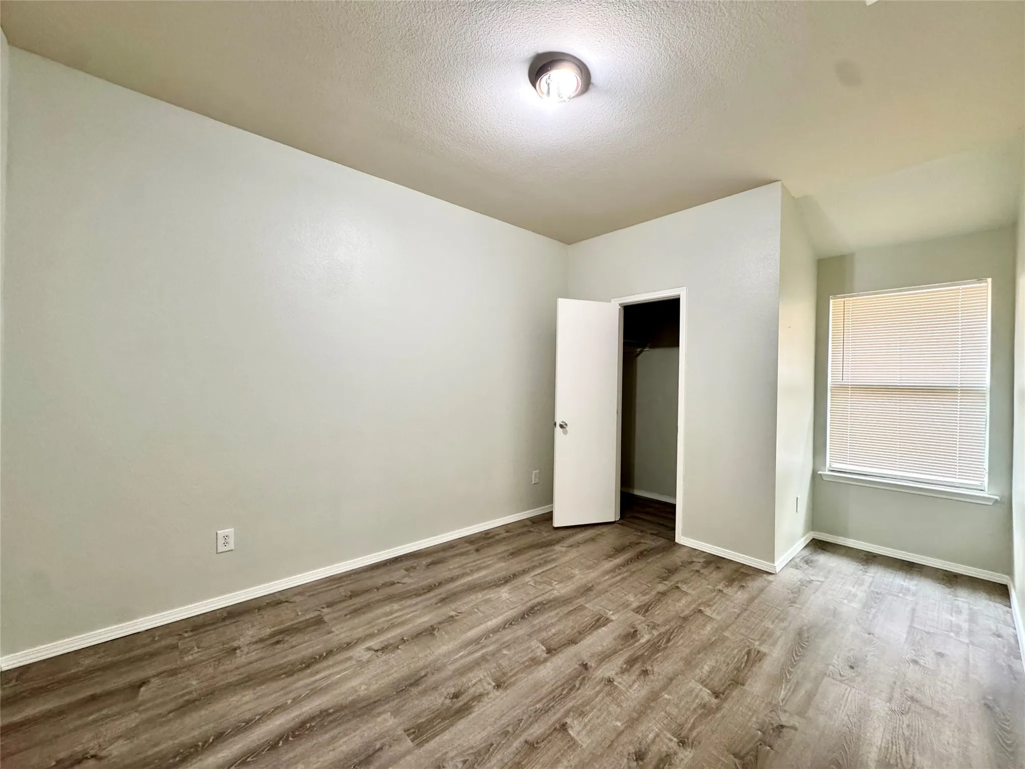 Wood-finish flooring, recessed window with blinds, ceiling-mounted light fixture, built-in closet with interior shelving