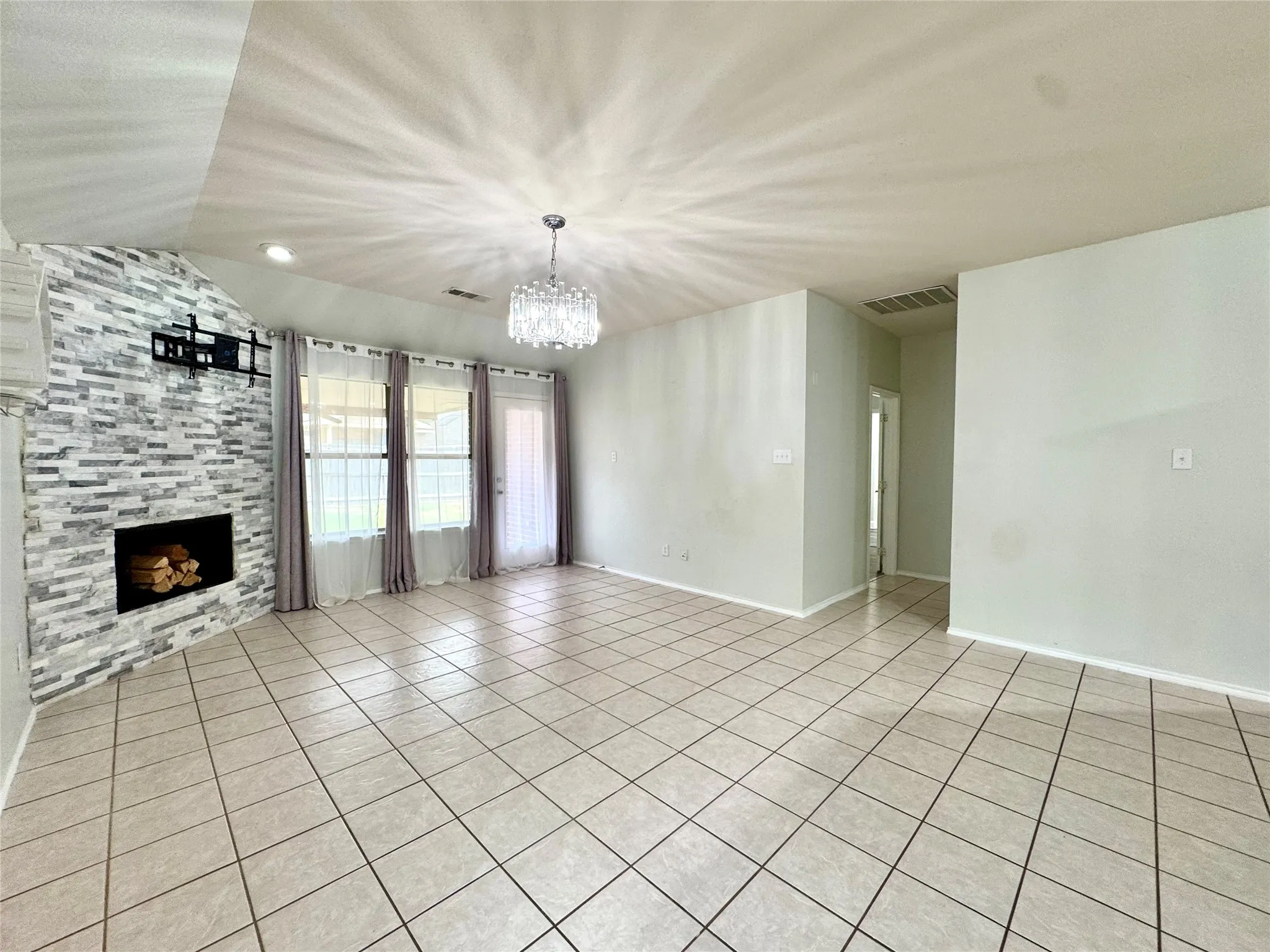 Tiled flooring throughout, modern chandelier, fireplace with stone surround, recessed lighting, and multiple windows