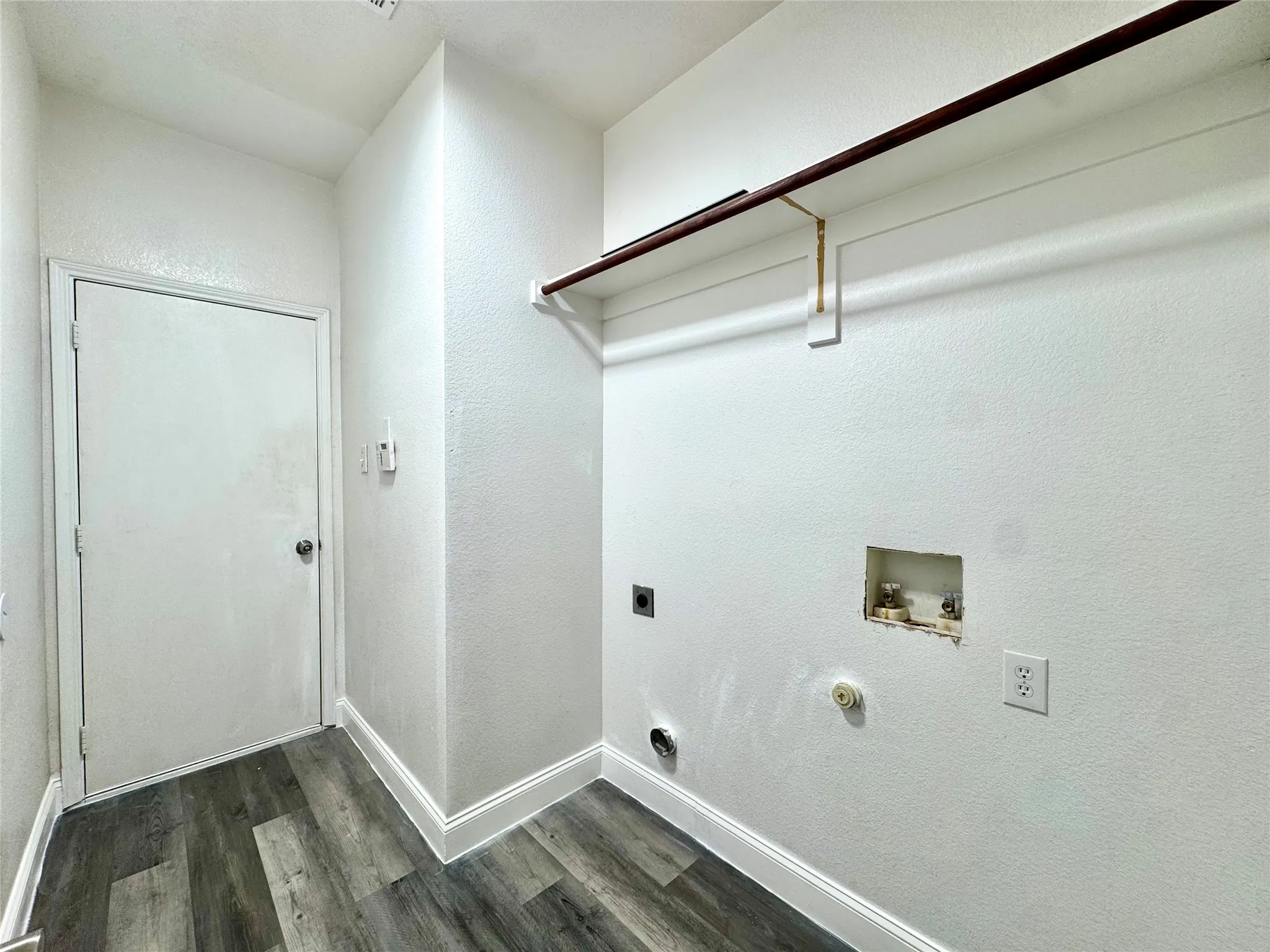 Laundry area featuring wood-finish flooring, white baseboards, a built-in shelving unit with a hanging rod, and a utility hook-up