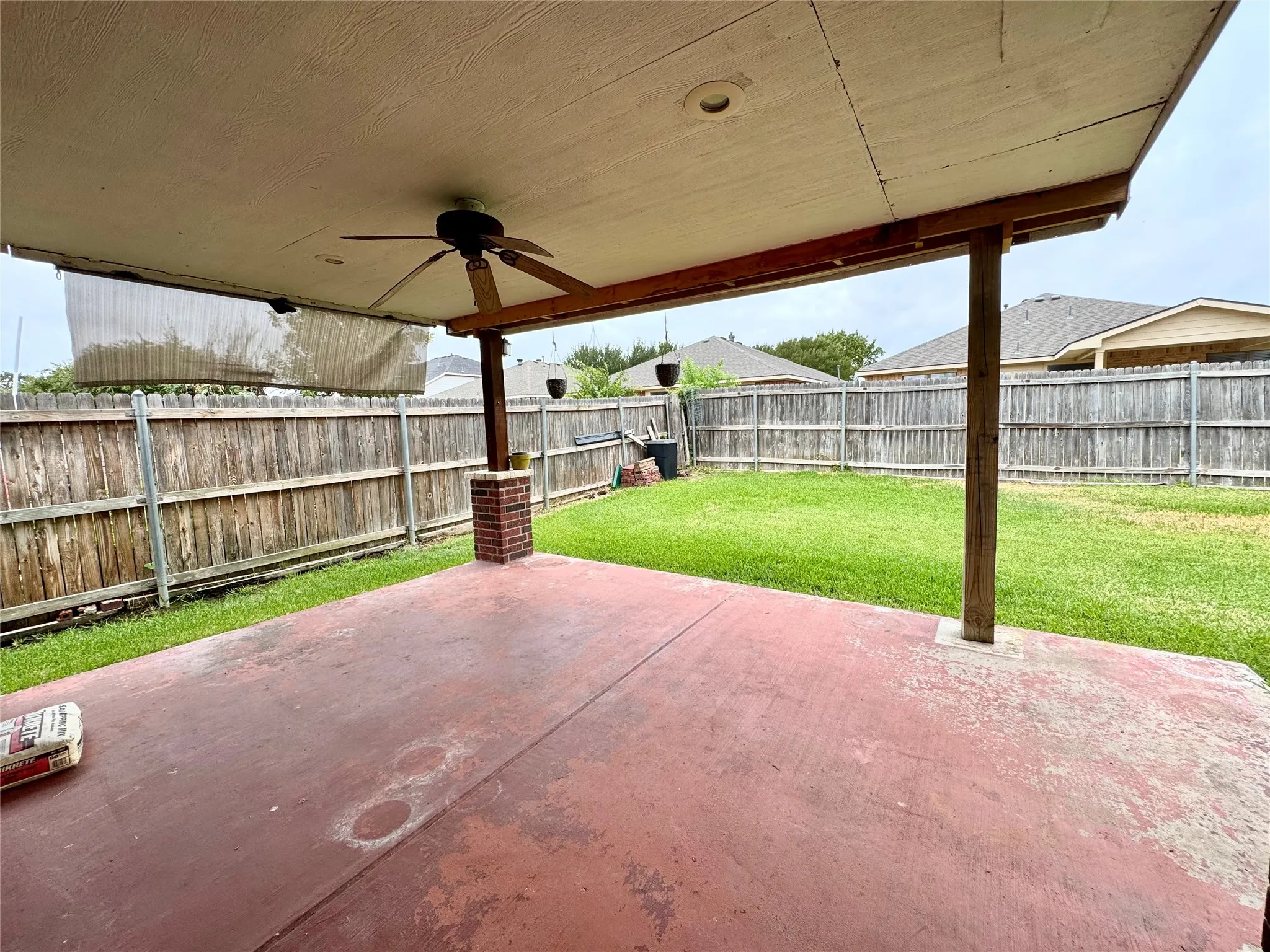 Covered patio with an integrated ceiling fan and recessed lighting, featuring a brick column accent and a fenced backyard with a grass lawn
