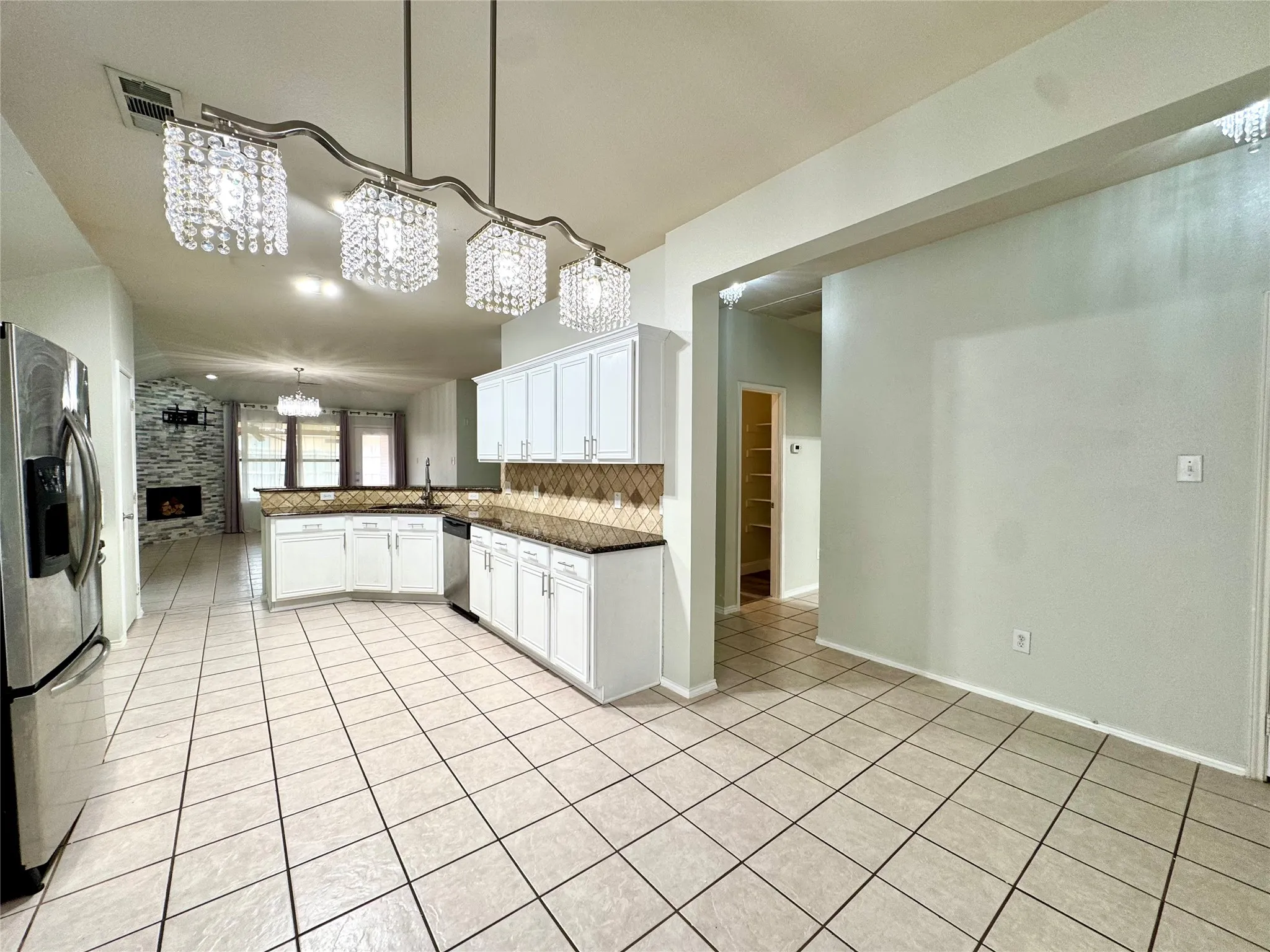 Open-concept kitchen featuring white cabinetry, dark countertops, a patterned tile backsplash, and stainless steel appliances