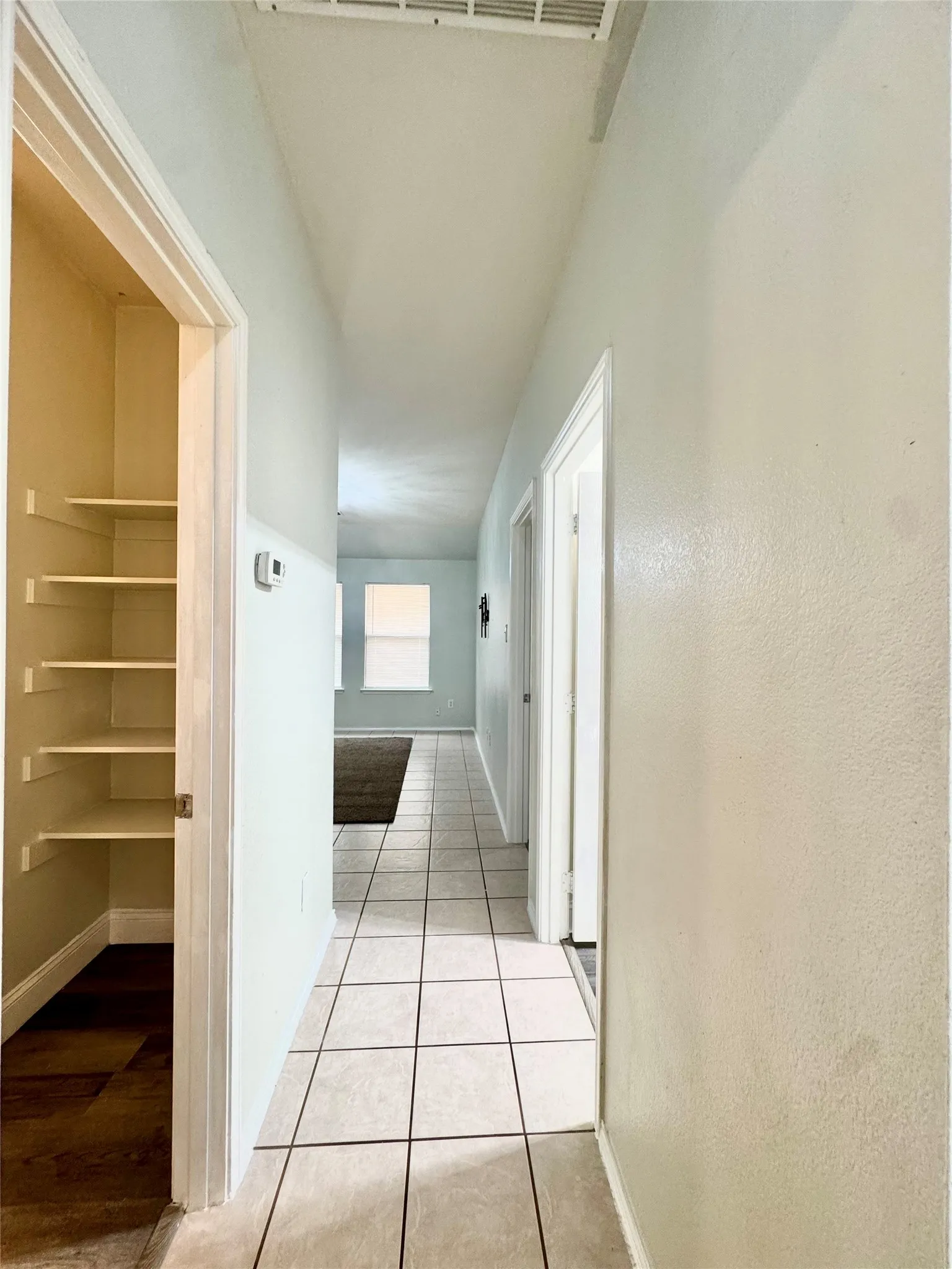 Hallway featuring light-toned tile flooring, built-in shelving, and white trim