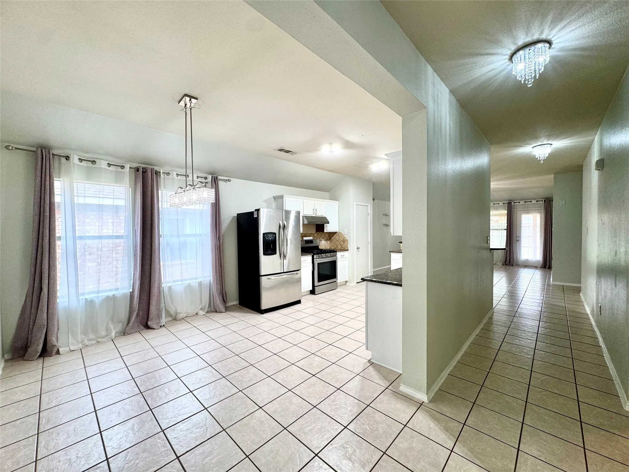 Tile flooring, stainless steel appliances, white cabinetry, ceiling-mounted chandelier, and recessed lighting
