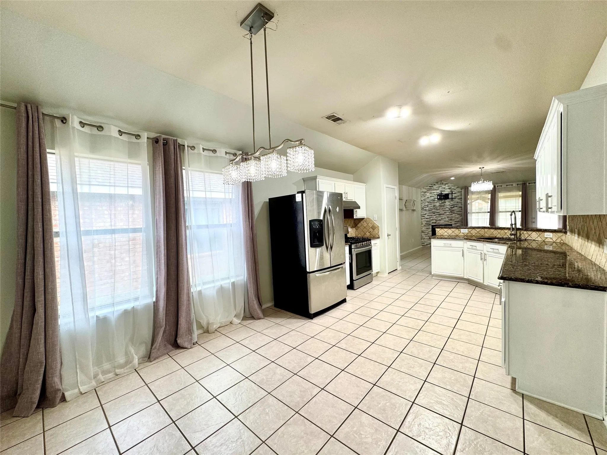 Tile flooring throughout, stainless steel appliances, white cabinetry, dark stone countertops, and a decorative tile backsplash
