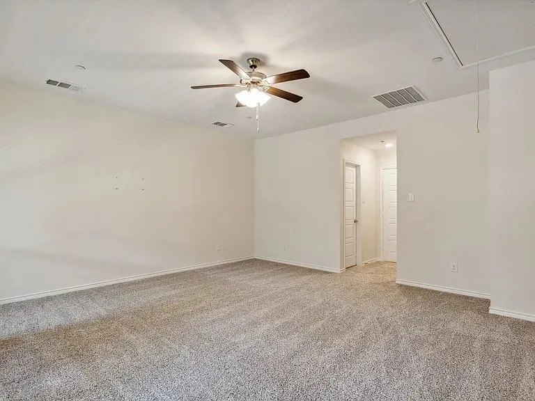 Unfurnished room featuring a ceiling fan, visible vents, attic access, and light colored carpet