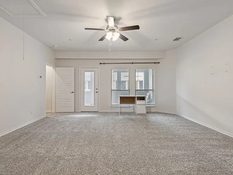 Unfurnished living room with carpet floors, a ceiling fan, attic access, baseboards, and visible vents