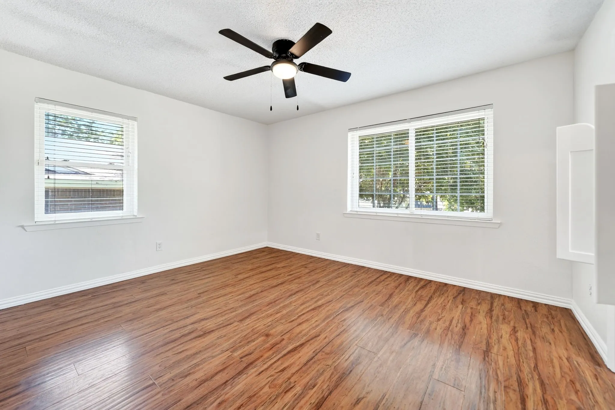 Wood-finish flooring, white walls, two windows with blinds, and a ceiling fan with integrated lighting