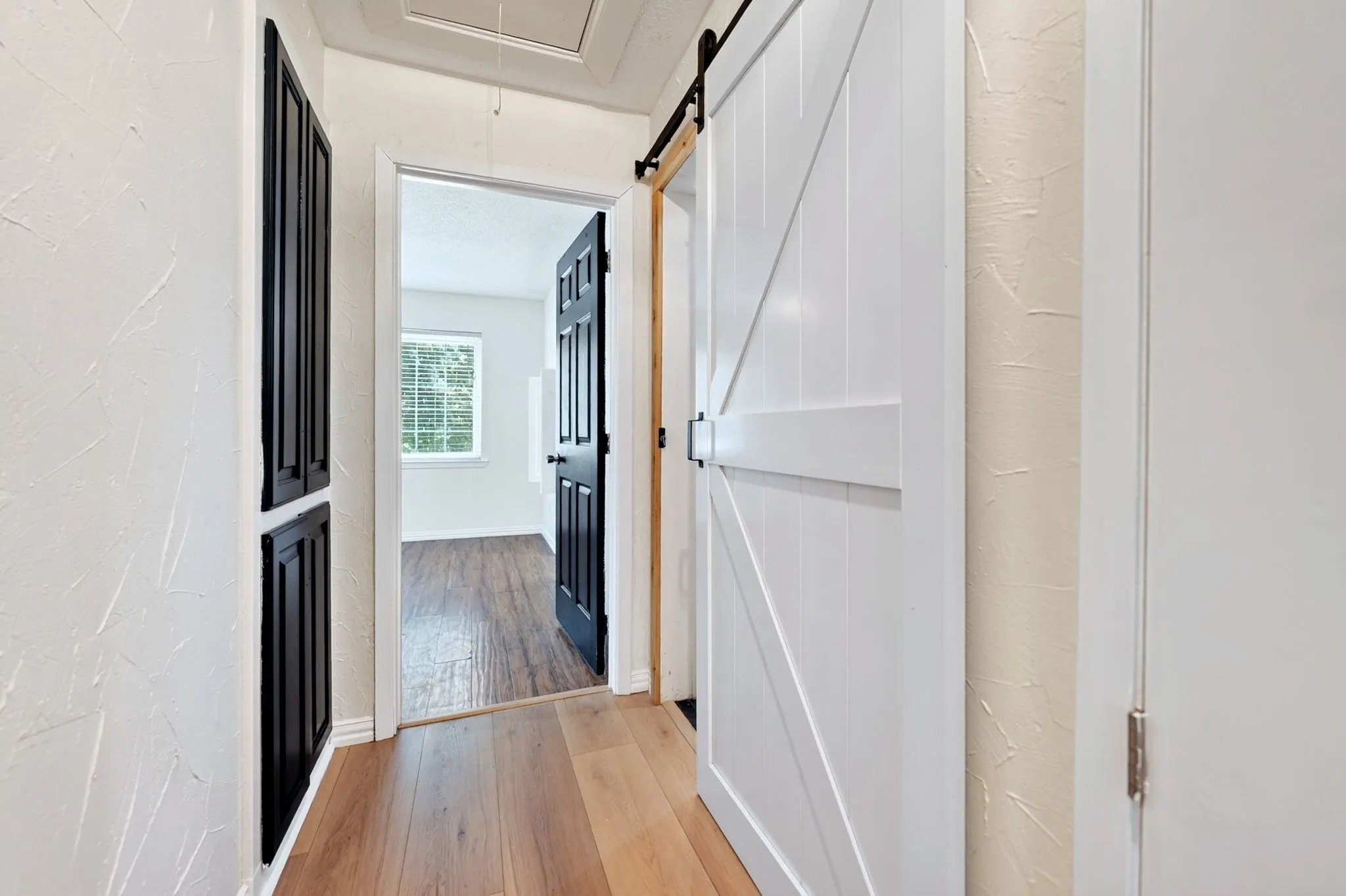 Hallway featuring wood-finish flooring, white textured walls, and a white barn door with black hardware
