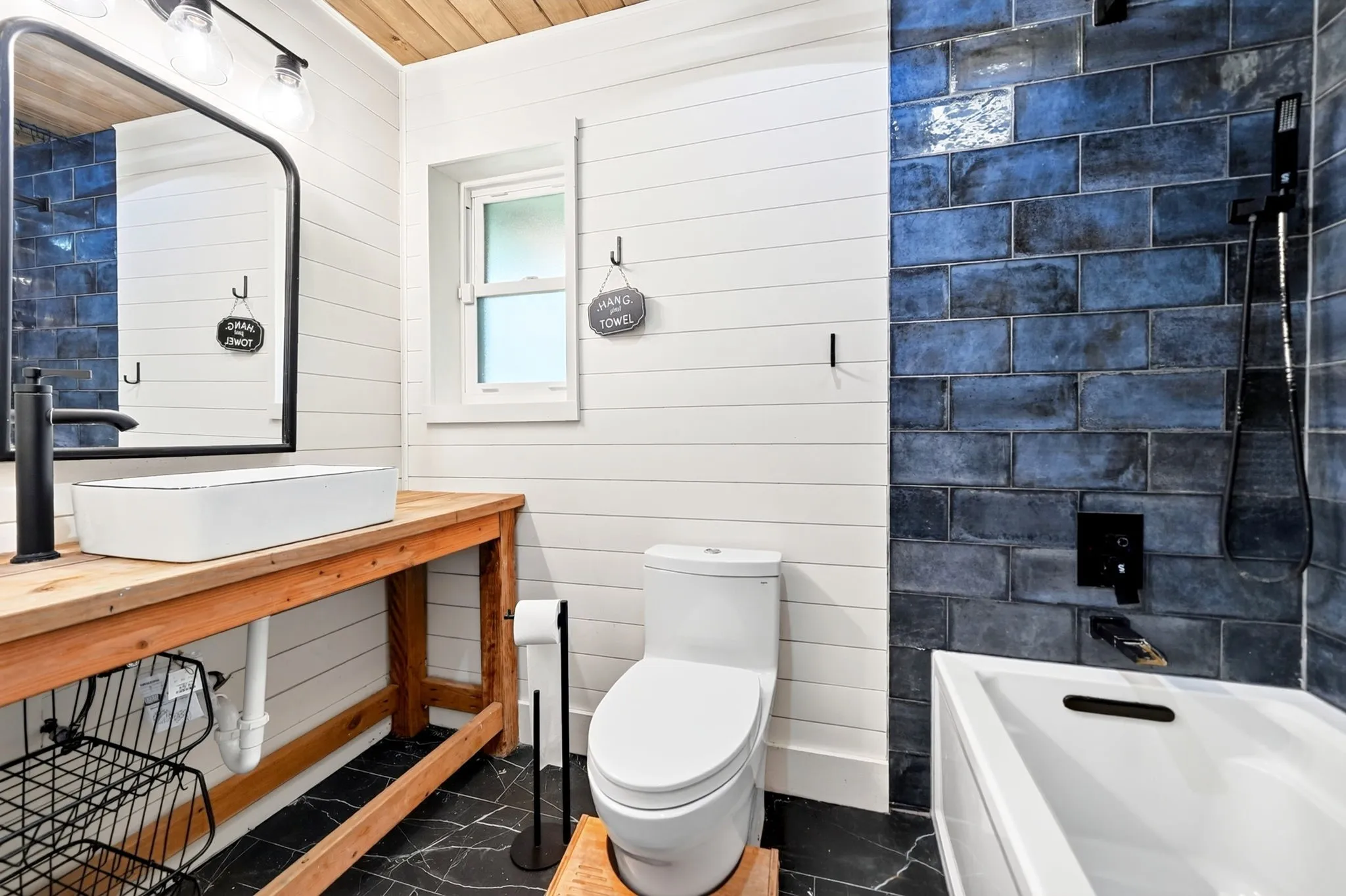 Shiplap wall paneling, blue subway tile shower surround, wood ceiling, rectangular vessel sink, and black-framed mirror