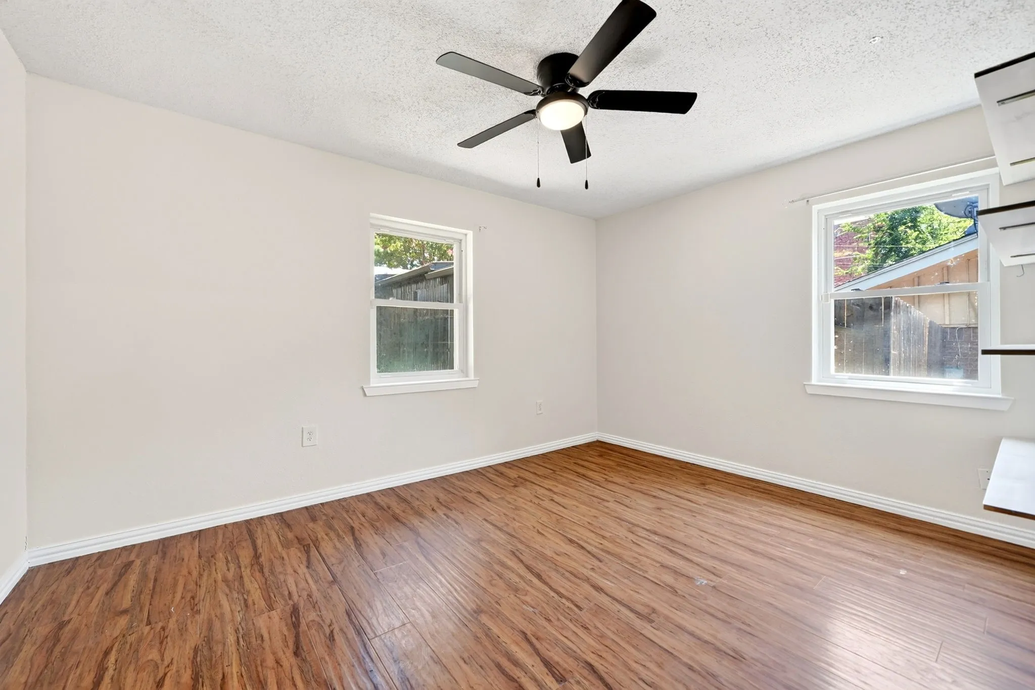Wood-finish flooring throughout, bright white walls, and a ceiling fan with integrated lighting