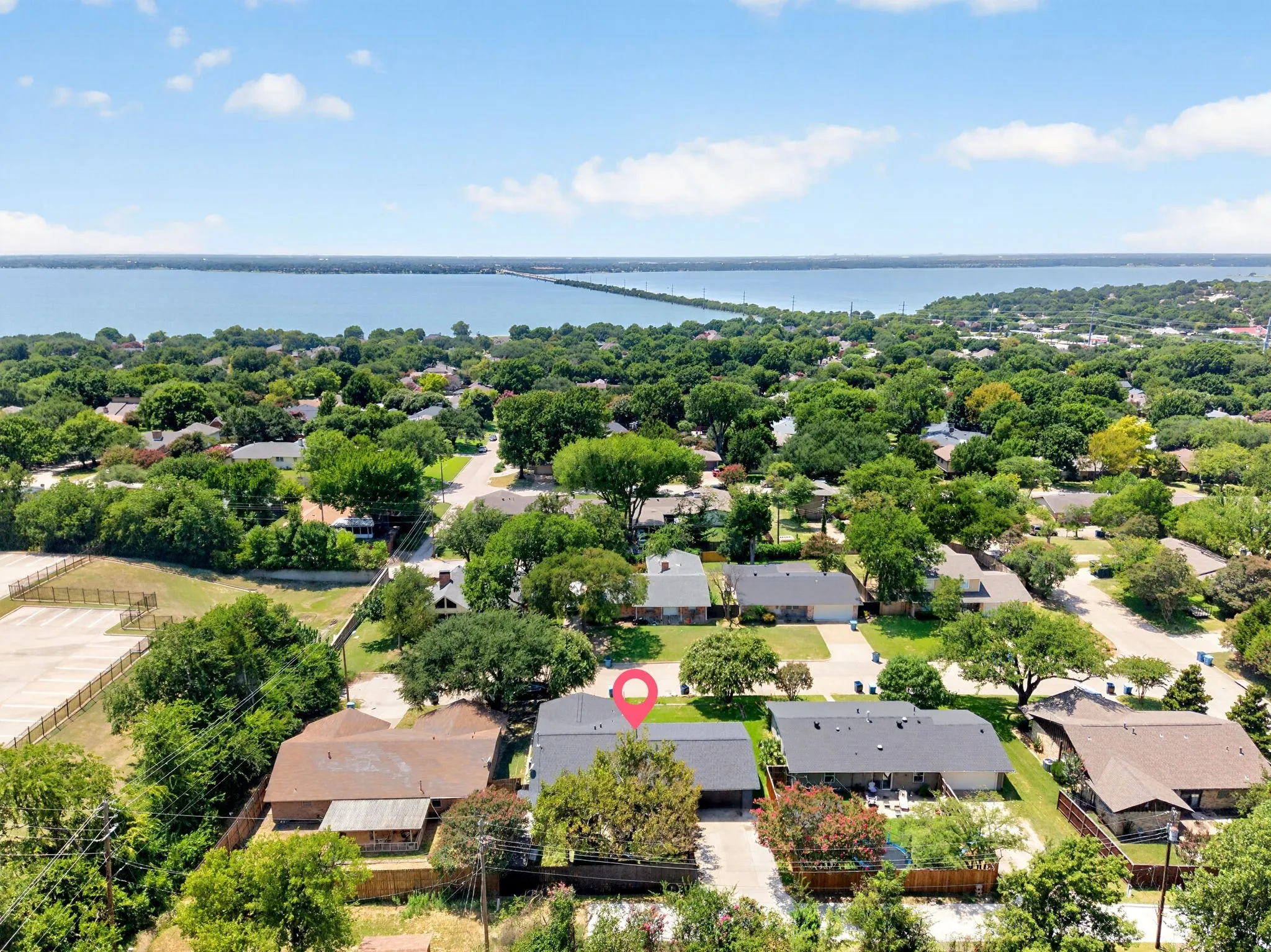 Aerial perspective showcasing a residential neighborhood with mature trees and a large body of water in the background