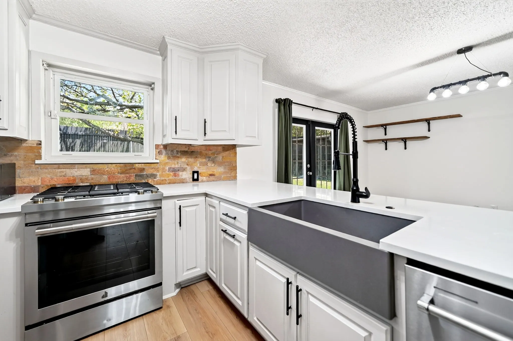 White cabinetry with black hardware, stainless steel appliances, stone backsplash, white countertops, and a gray farmhouse sink