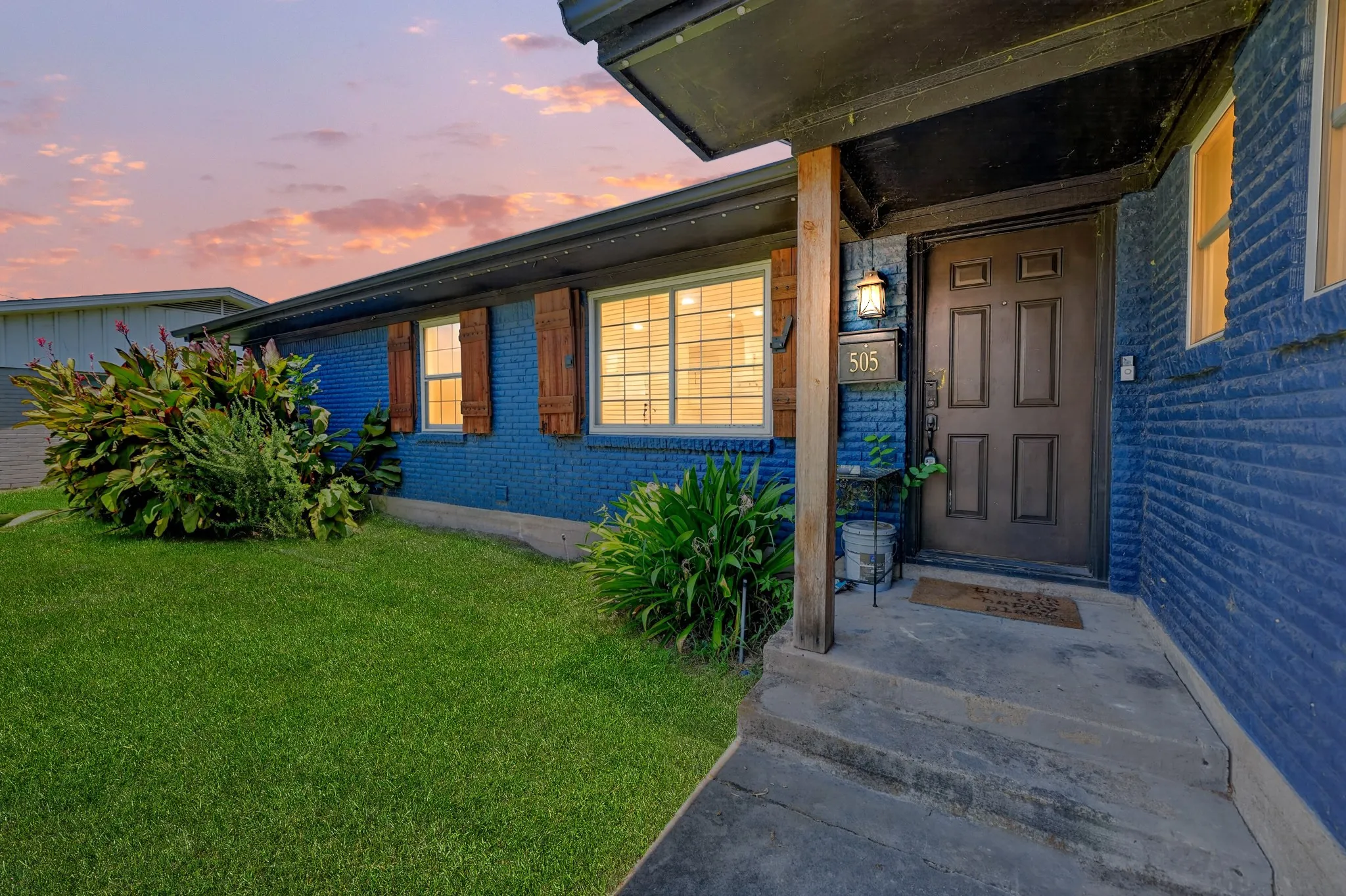 Exterior featuring blue brick siding, a covered entry, wood-paneled door, and decorative window shutters
