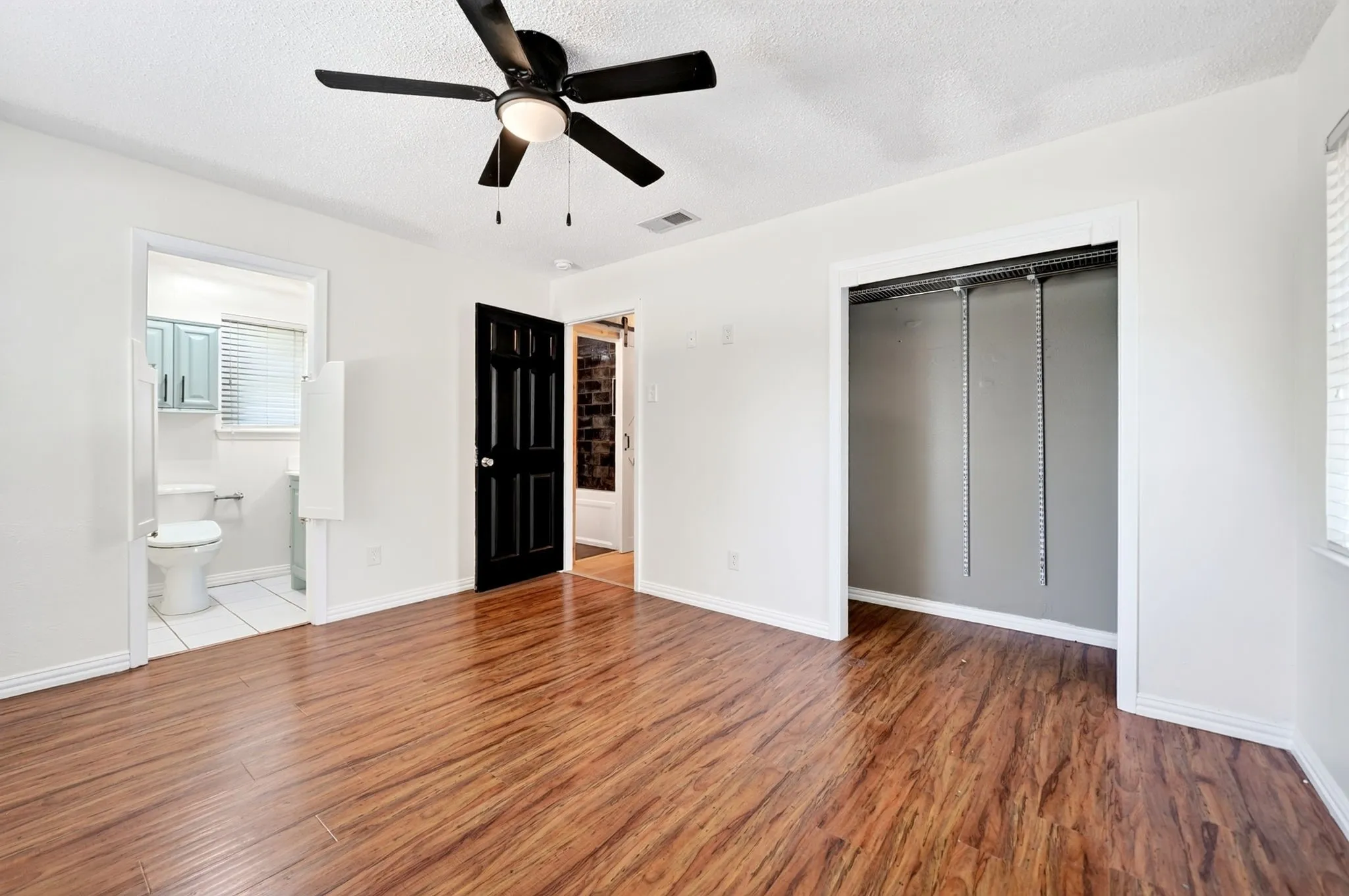 Wood-finish flooring, ceiling fan with integrated lighting, open closet with hanging rods, white walls, and a full bathroom with light blue cabinetry