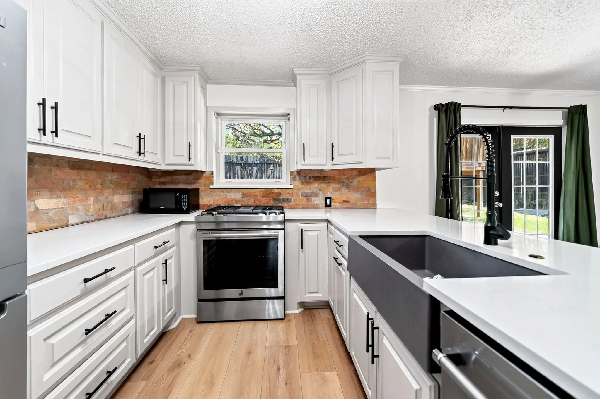 White shaker cabinetry, light wood-finish flooring, stainless steel appliances, brick-style backsplash, and a matte black farmhouse sink