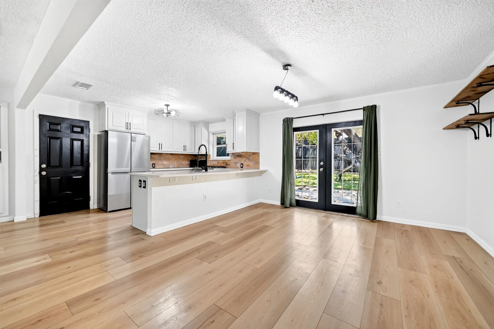 Open-concept kitchen and living area featuring wood-finish flooring, white cabinetry, and stainless steel appliances