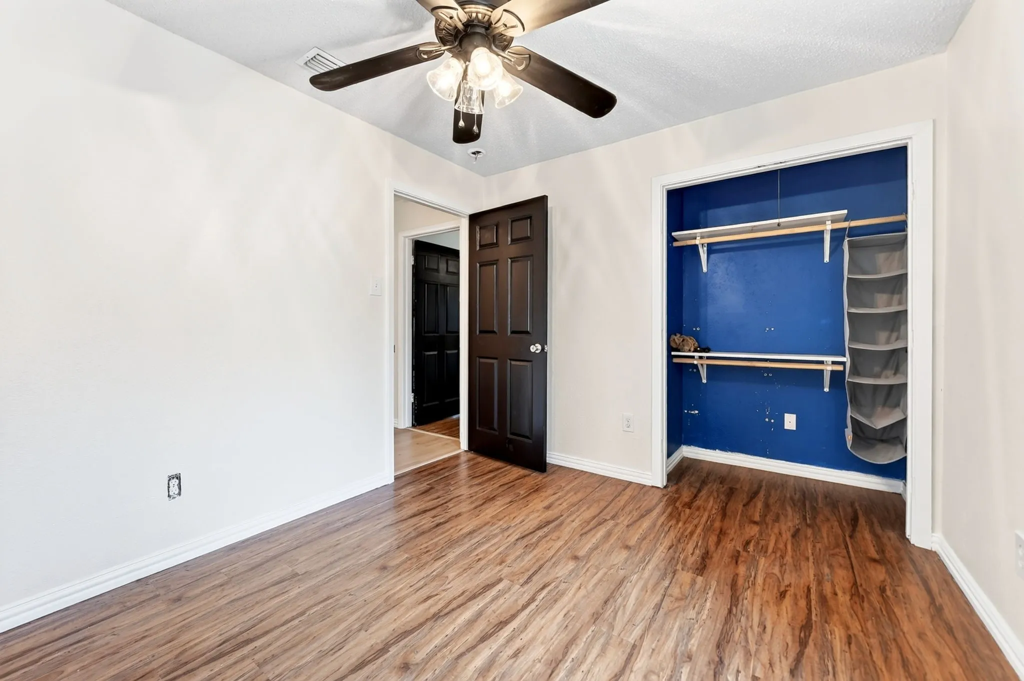 Wood-finish flooring throughout, ceiling fan with integrated lighting, and a built-in closet with shelving