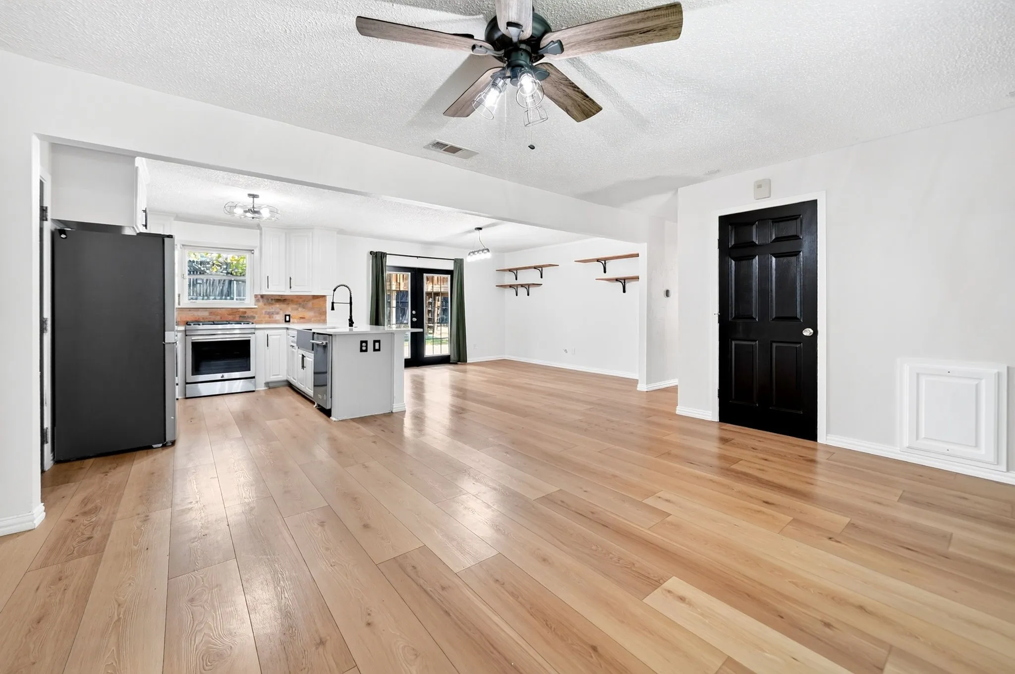 Hardwood-style flooring throughout, kitchen with white cabinetry and island, stainless steel appliances, and a wood-look backsplash