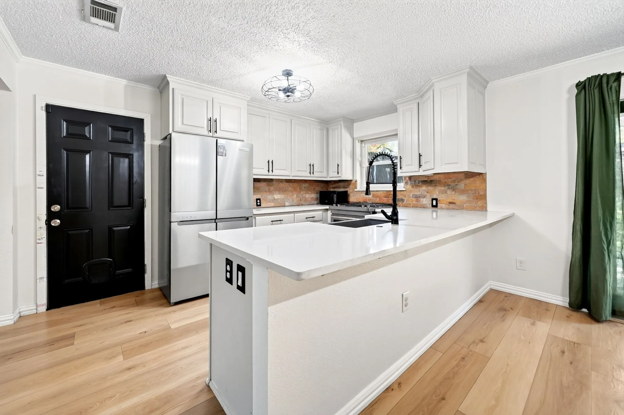 Kitchen featuring light-tone wood-finish flooring, white cabinetry with black hardware, white countertops, and a brick-finish backsplash