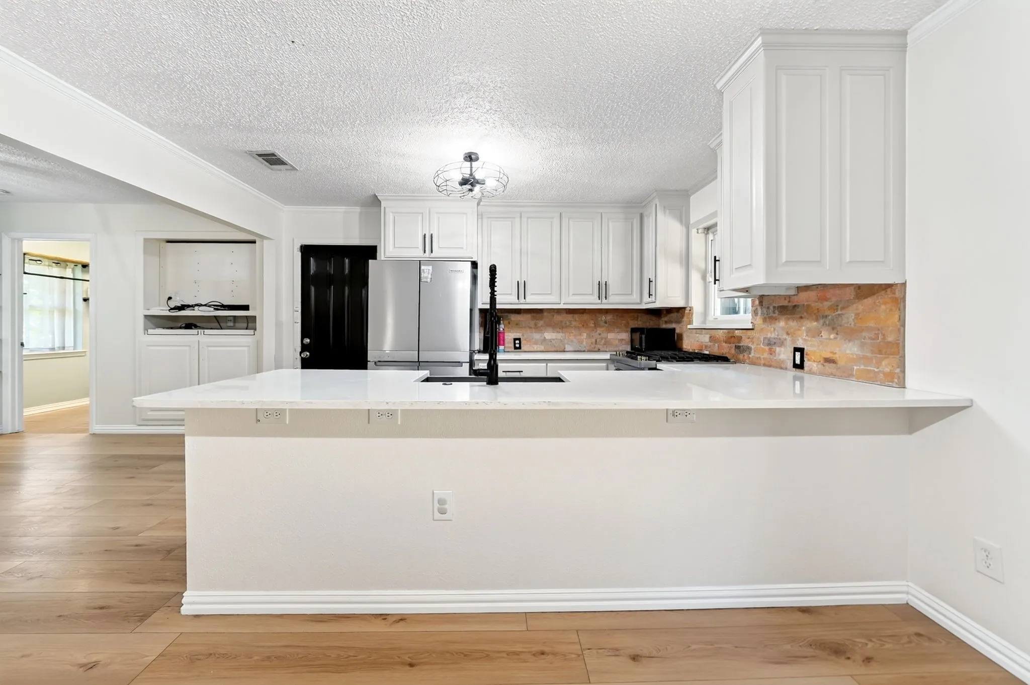 Kitchen featuring white shaker cabinetry, light-toned wood-finish flooring, a white countertop, and a brick-pattern backsplash