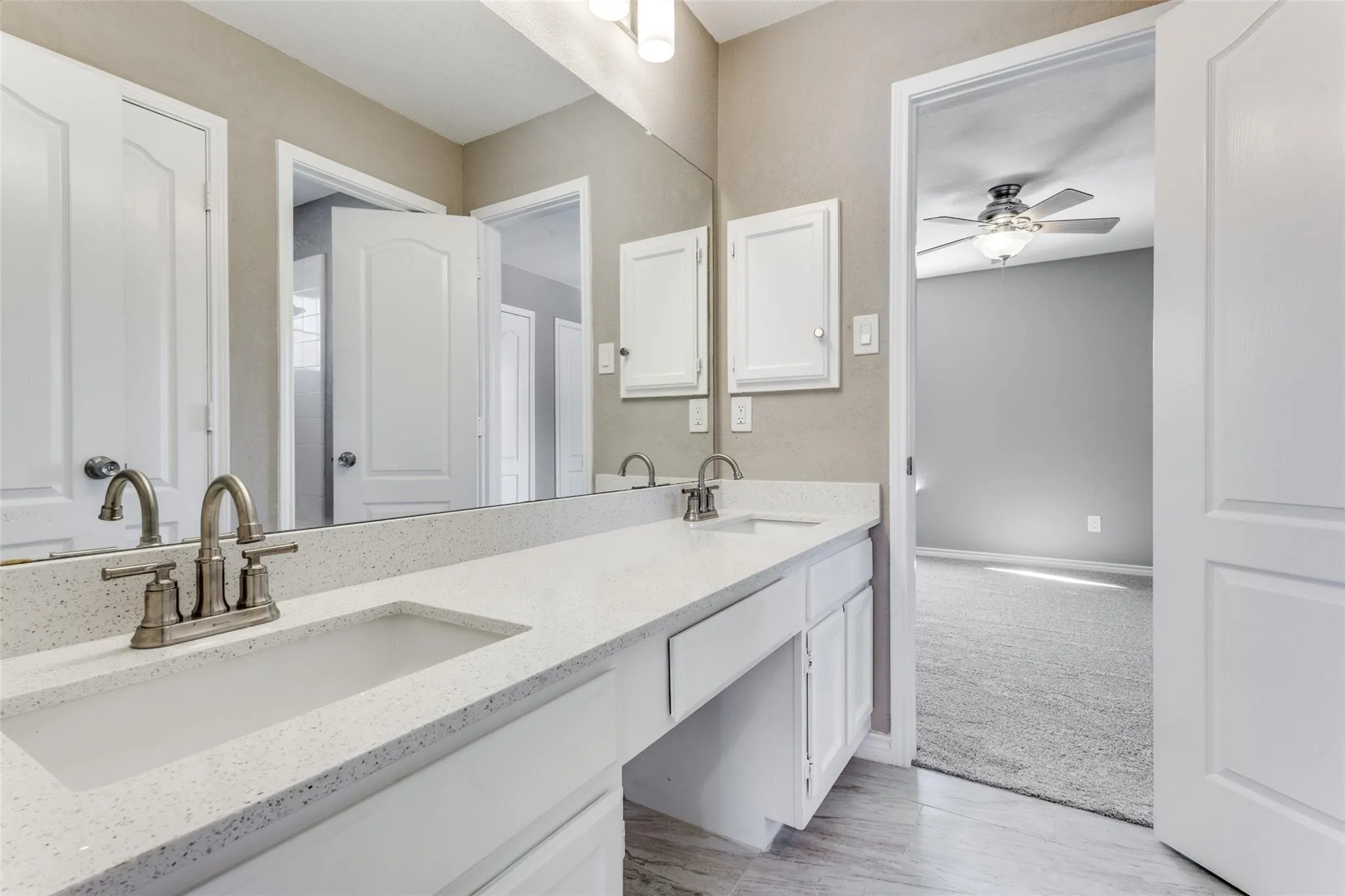 Dual vanity upstairs with integrated sinks, brushed nickel fixtures, white cabinetry, and a full-width mirror