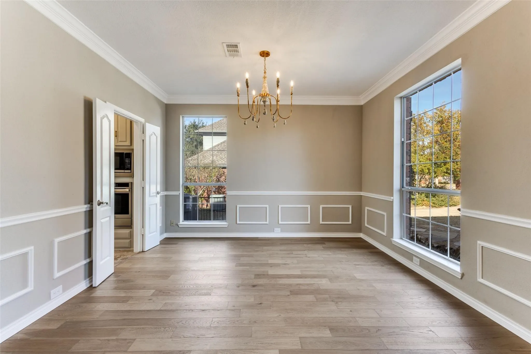 Wood-finish flooring, decorative wall molding, large window, double doors, and a gold-tone chandelier