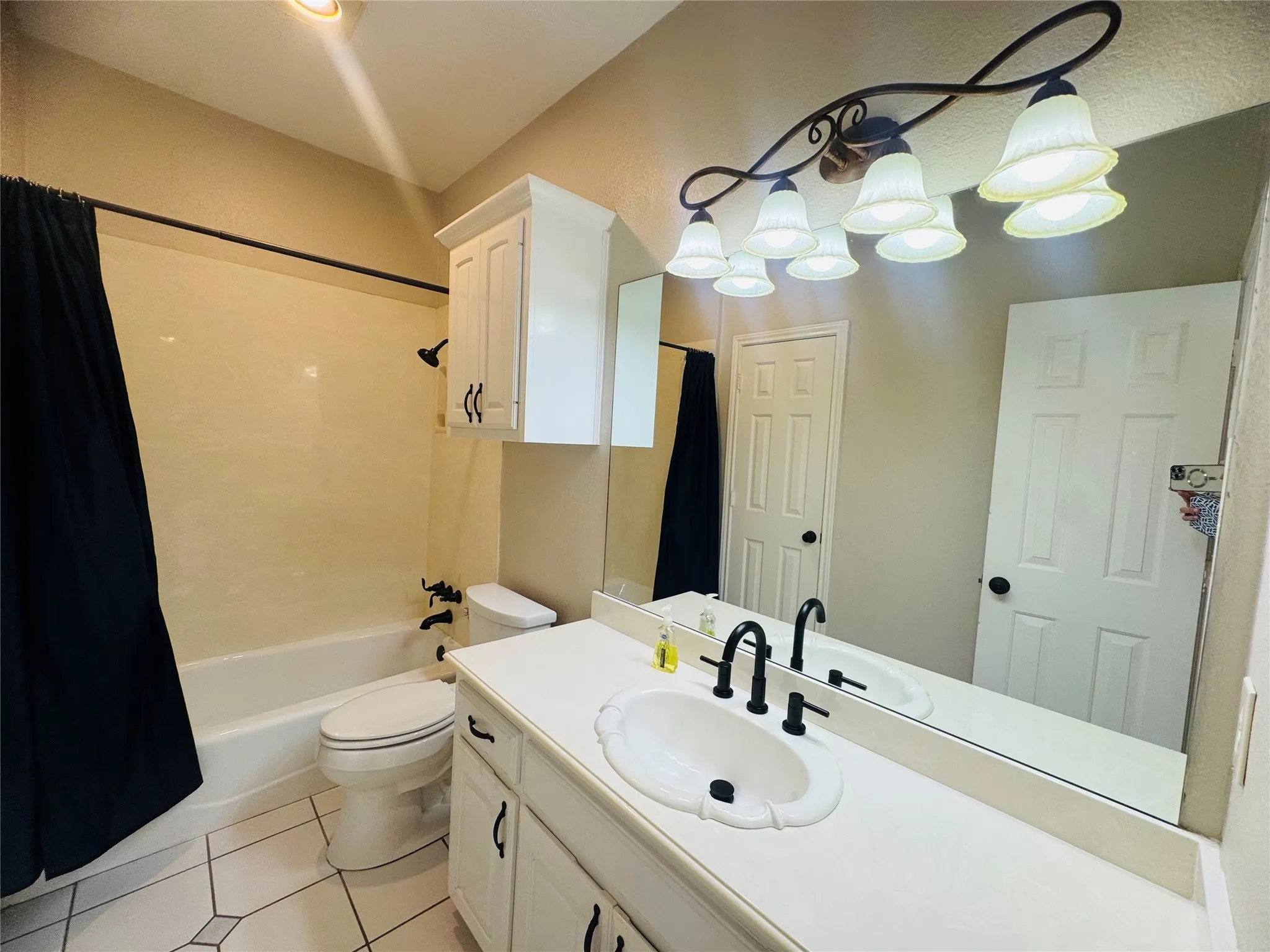 Bathroom featuring a white vanity with integrated sink, matte black faucet, wall-mounted mirror, and tile flooring