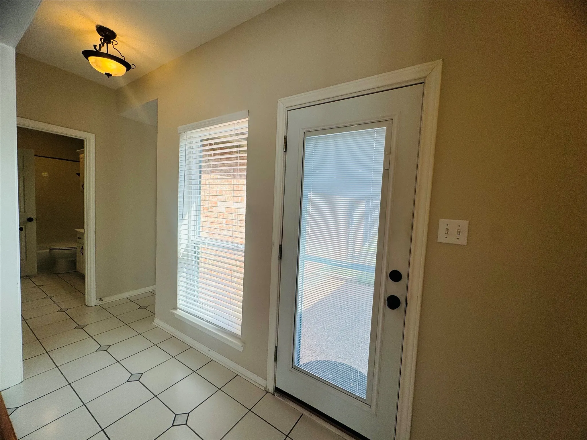 Tiled flooring with decorative accents, an exterior door with integrated blinds, and a large window with horizontal blinds