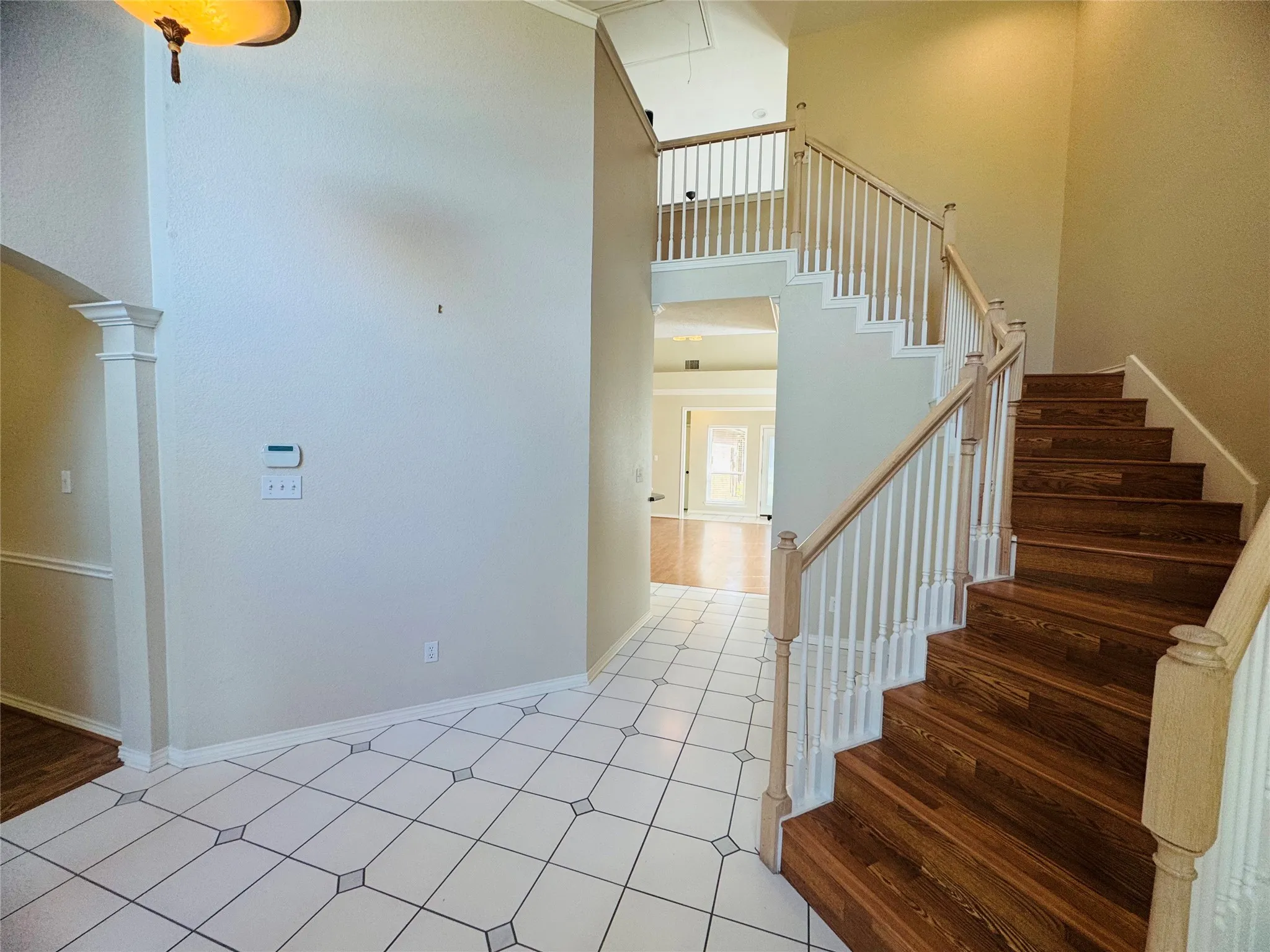 Two-story entryway featuring wood-finish staircase, white balusters, and square tile flooring with decorative inserts