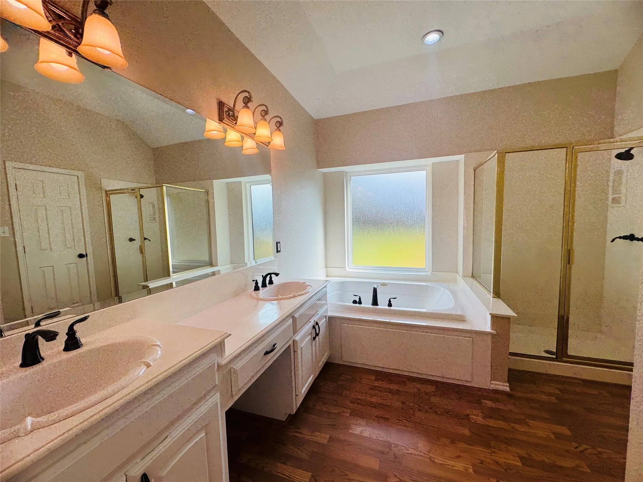 Dual vanity with integrated sinks, built-in soaking tub, separate shower enclosure, and wood-finish flooring