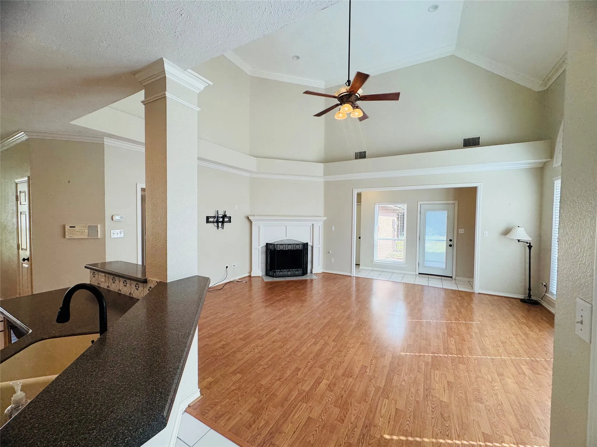 Vaulted ceiling with crown molding, wood-finish flooring, fireplace with white mantel, glass-paned exterior door, and built-in breakfast bar