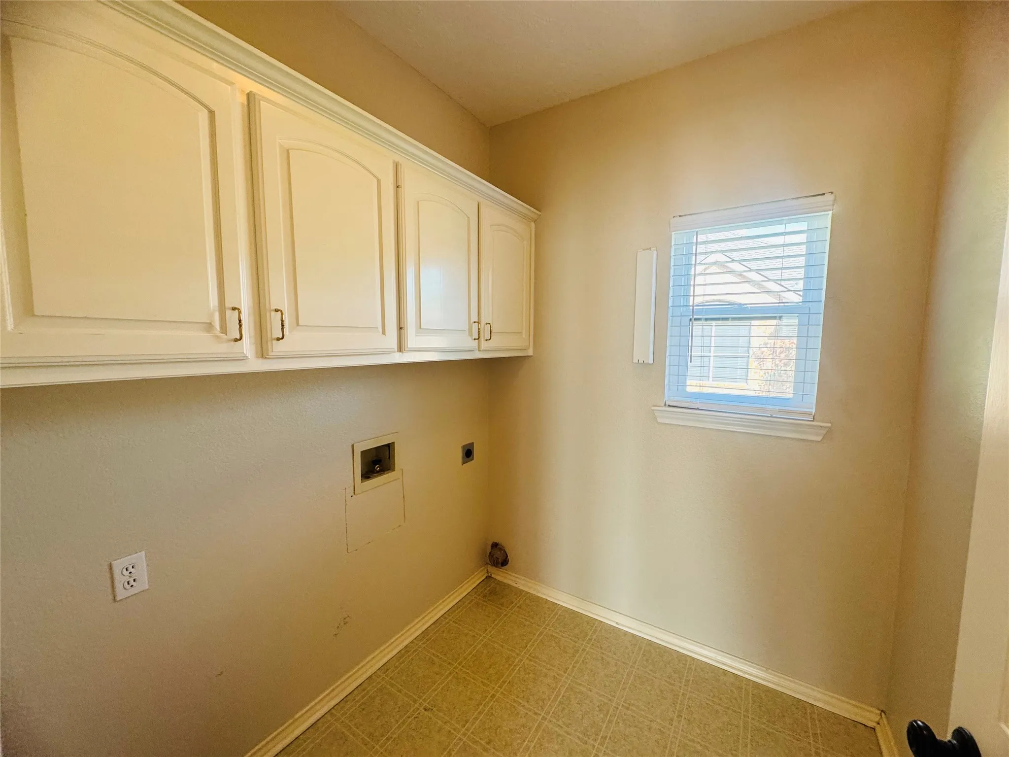 White upper cabinetry with arched panel doors, window with blinds, and durable sheet vinyl flooring