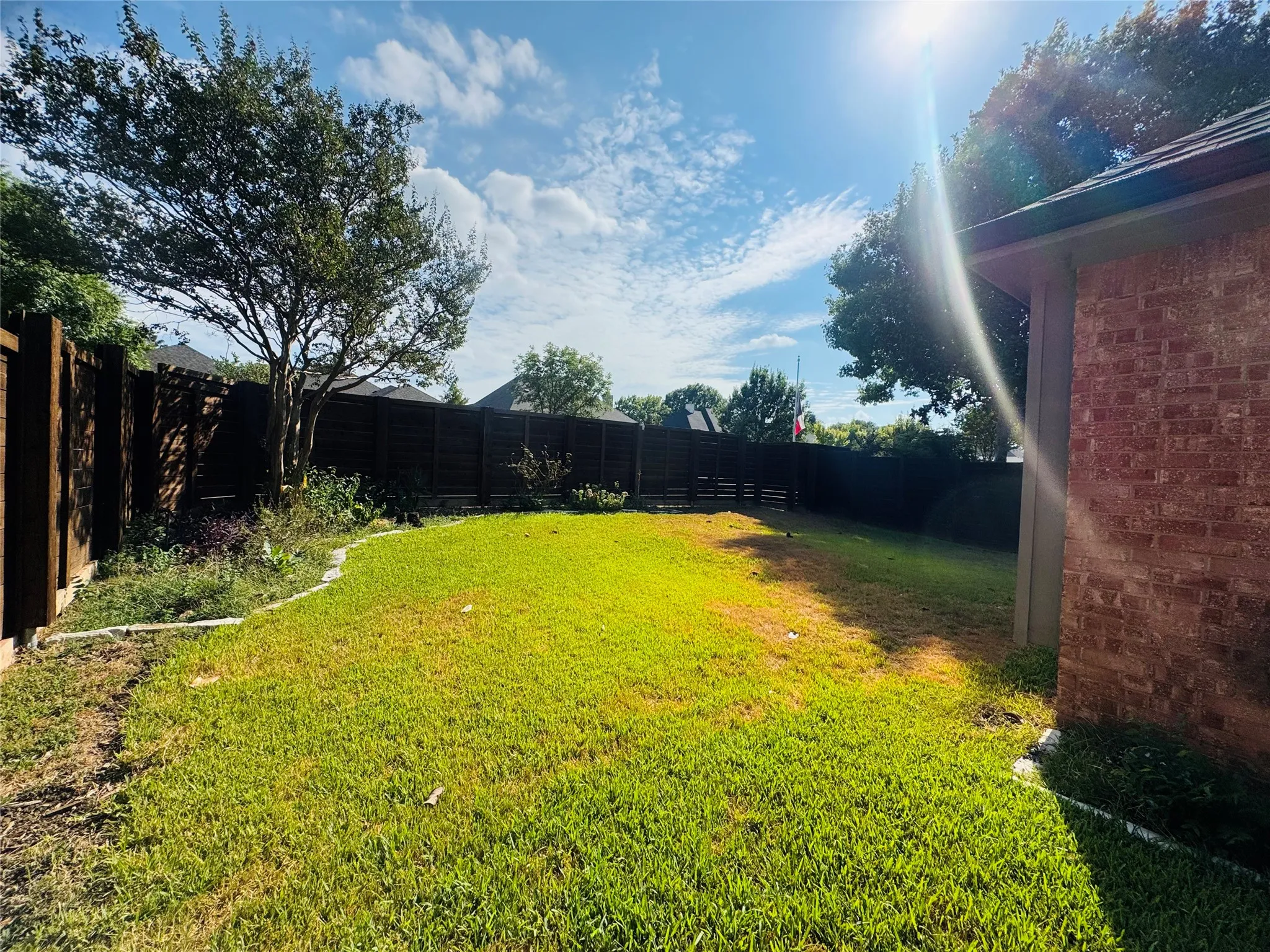 Expansive backyard featuring a manicured lawn, established trees, and perimeter fencing