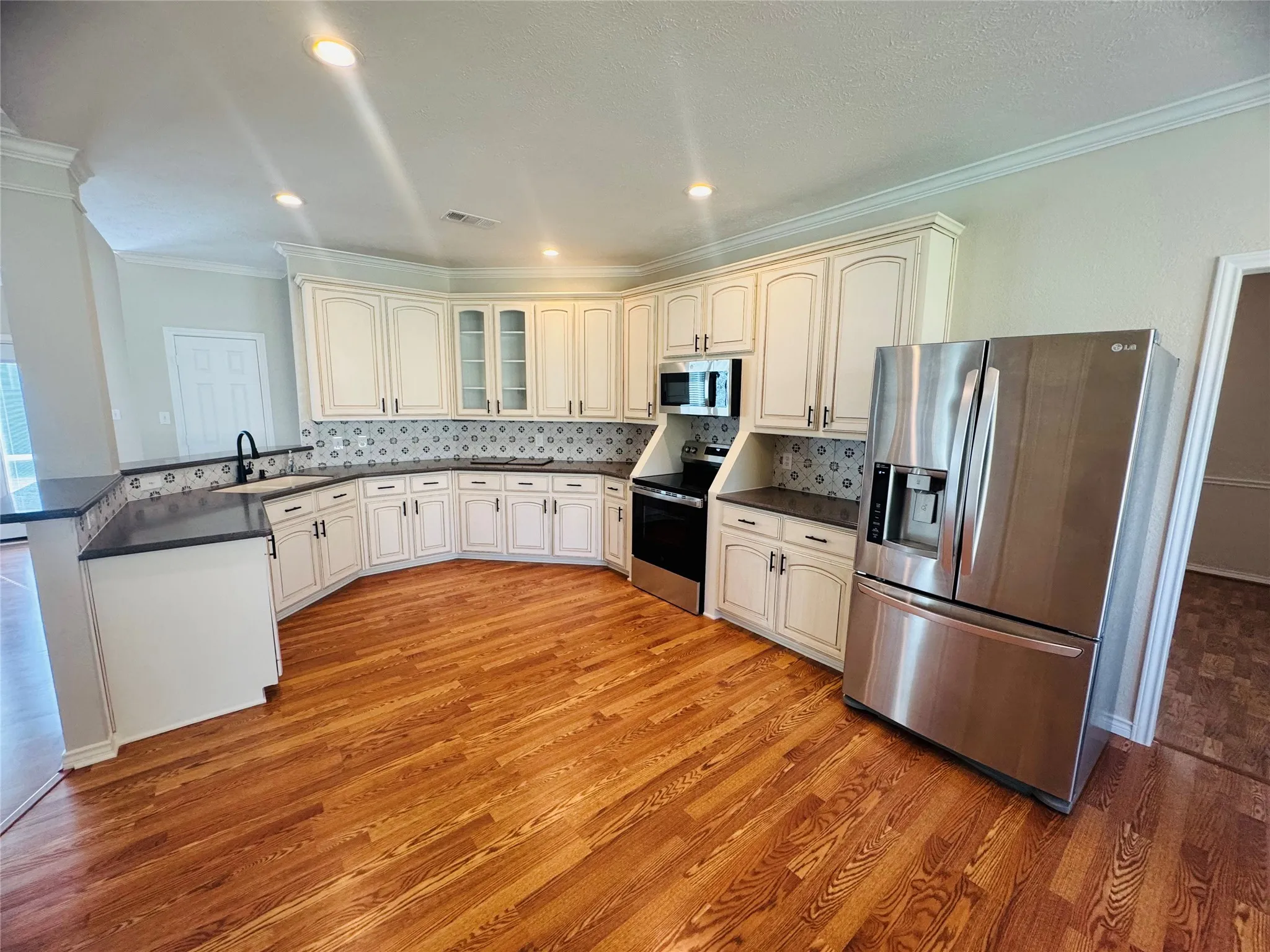 Kitchen featuring wood-finish flooring, recessed lighting, stainless steel appliances, white cabinetry, and a patterned backsplash