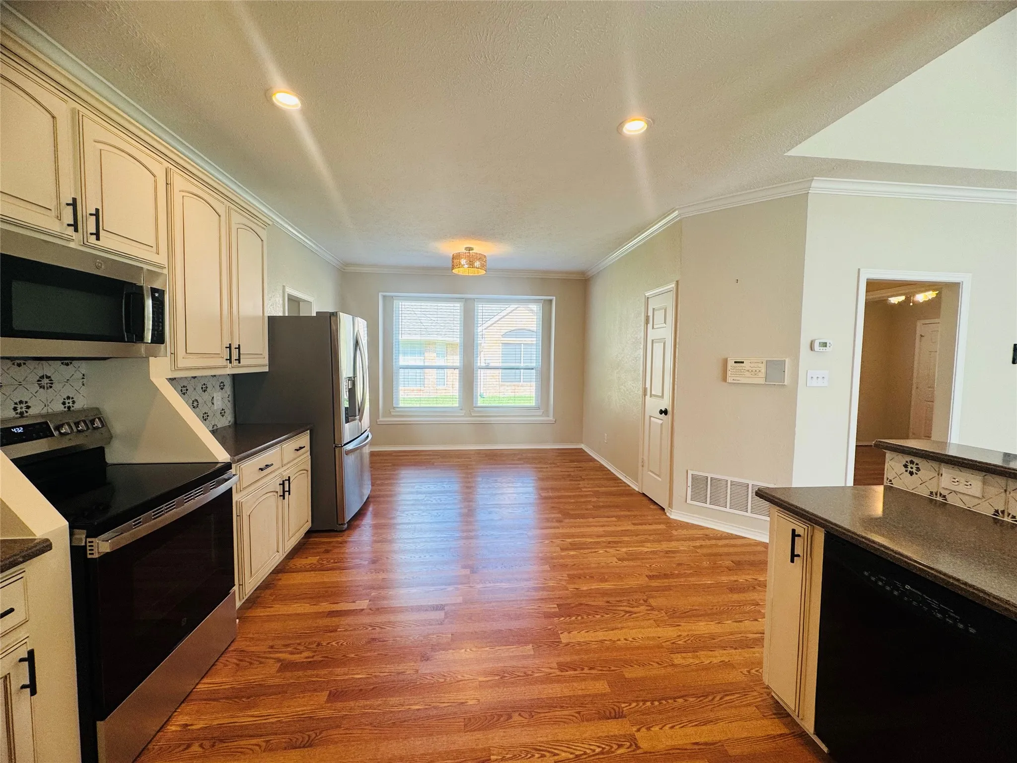 Kitchen featuring wood-finish flooring, white cabinetry, stainless steel appliances, and a tiled backsplash