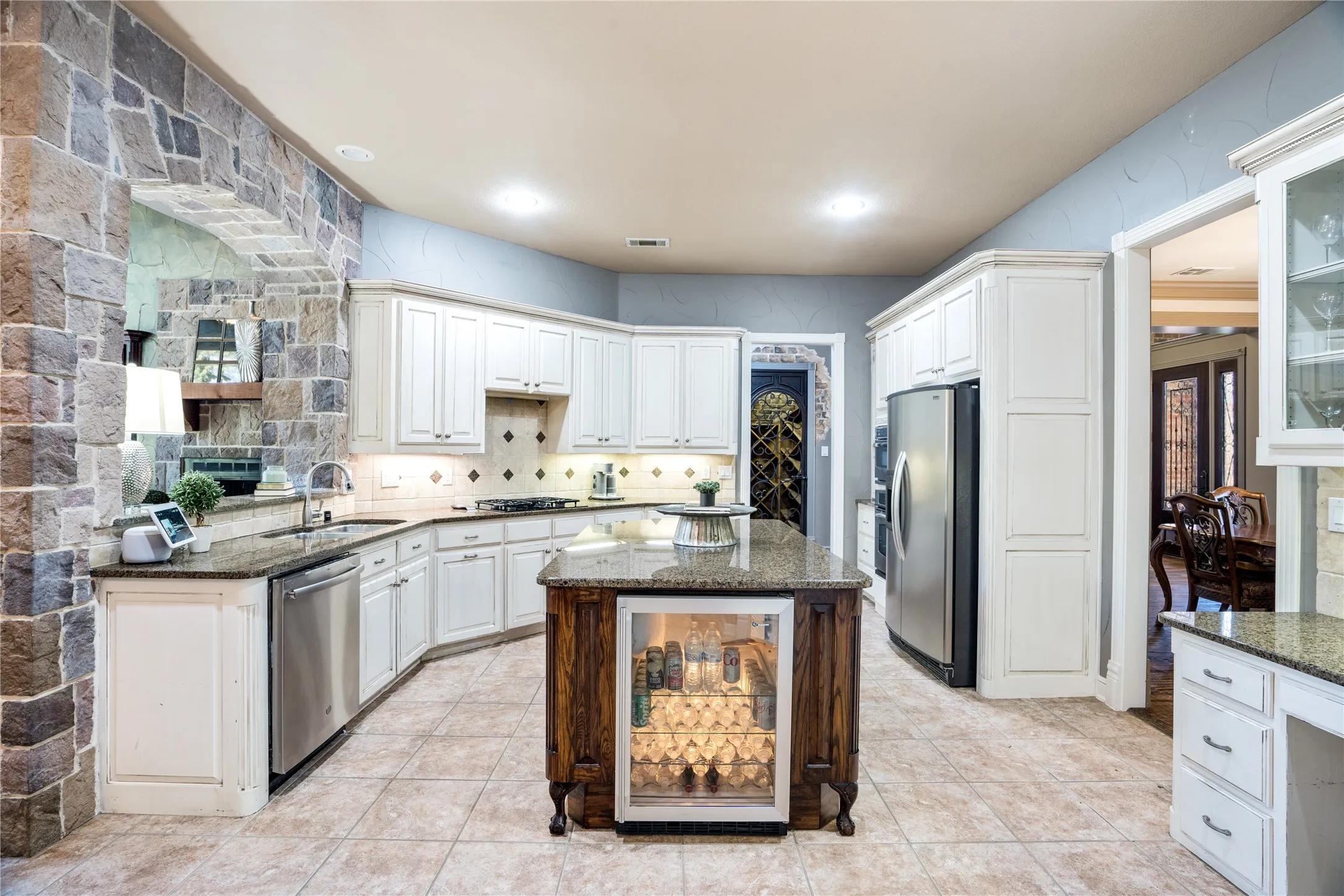 Expansive kitchen featuring stone accent wall, white cabinetry, integrated stainless steel appliances, and a central island with a built-in beverage cooler