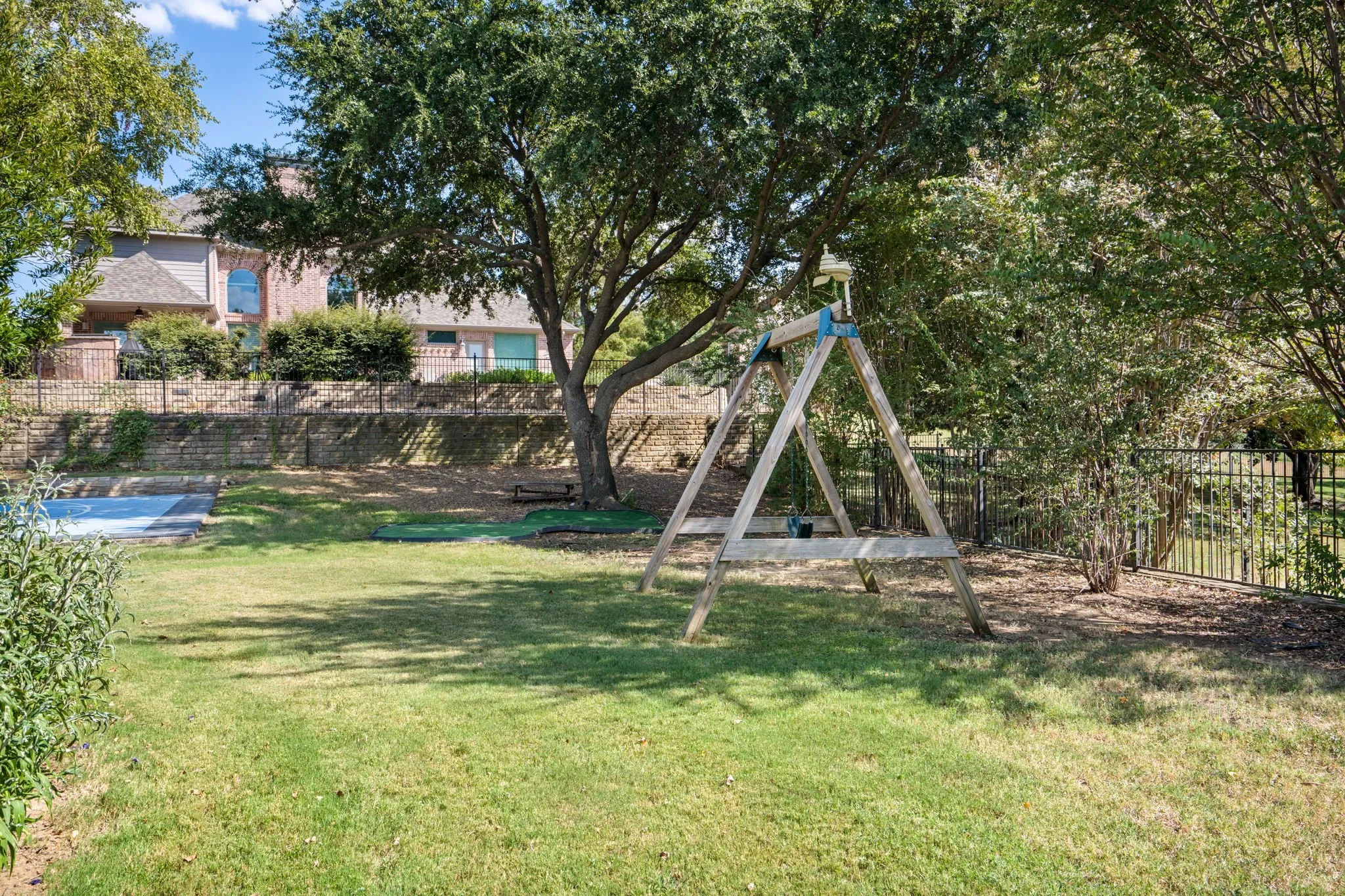 Expansive backyard featuring a manicured lawn, mature trees, and a black wrought-iron fence