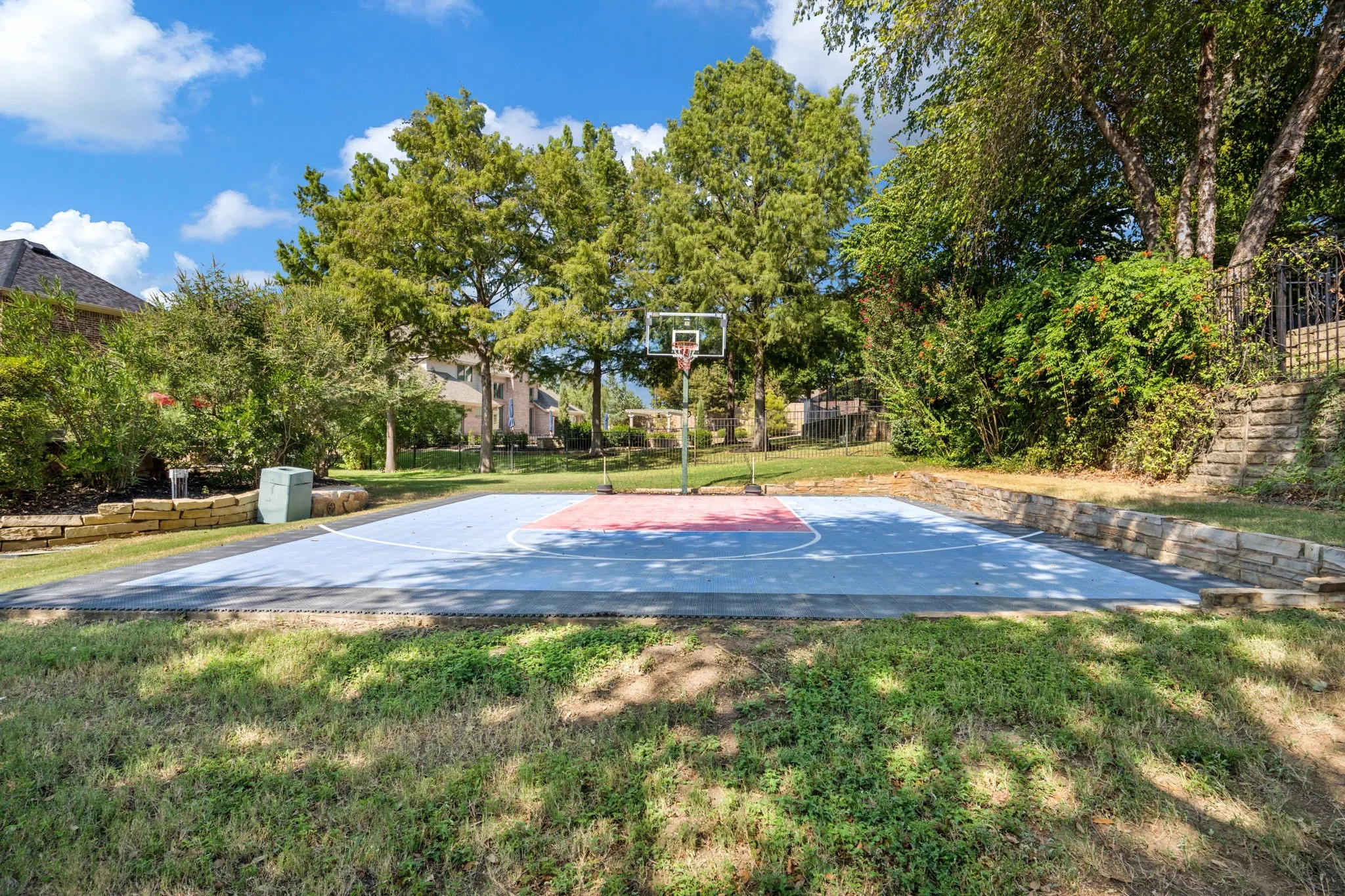 Full-sized sports court with retaining walls, surrounded by mature trees and lush landscaping