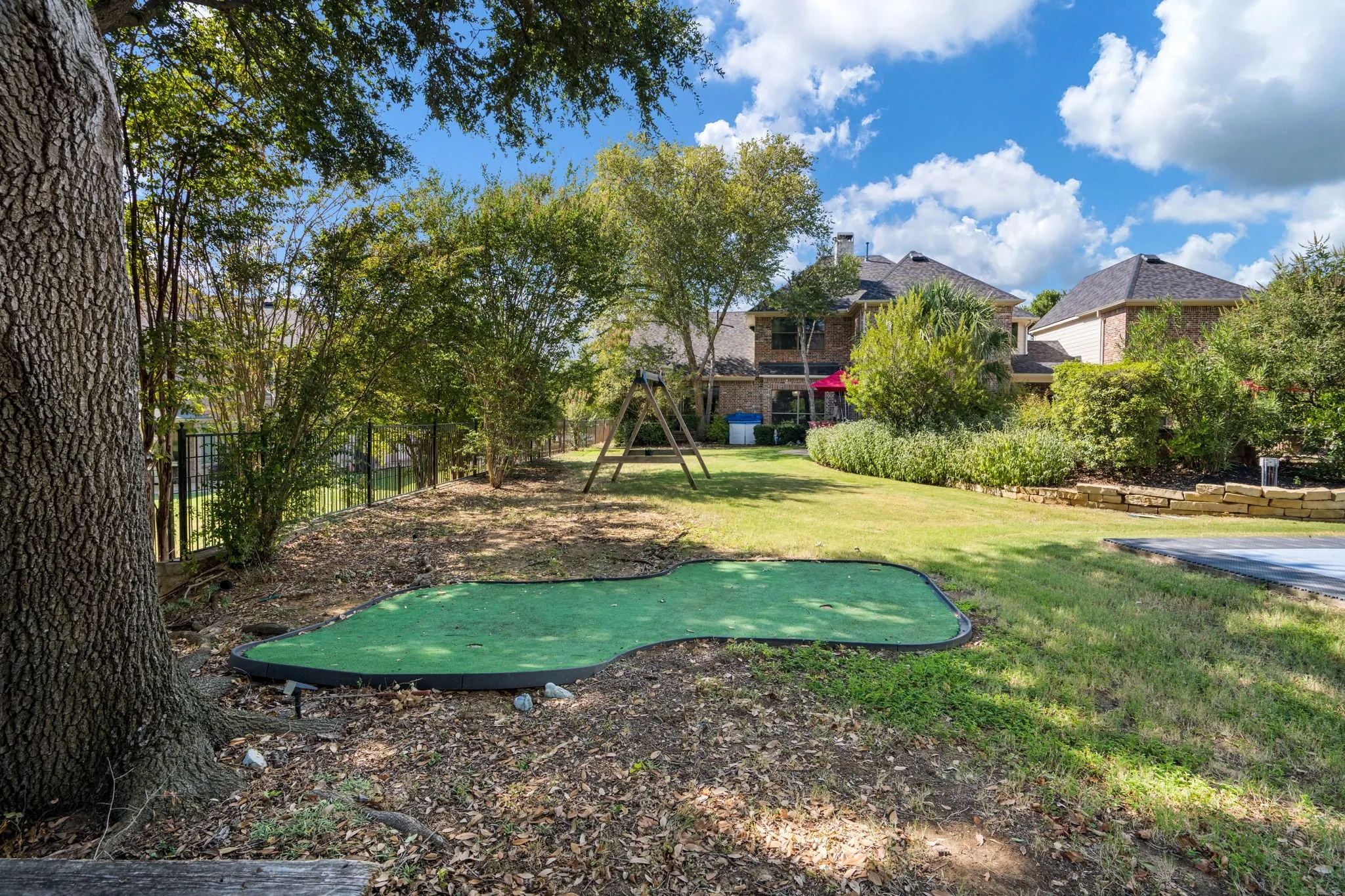 Expansive backyard featuring a putting green, mature trees, manicured lawn, and stone retaining wall