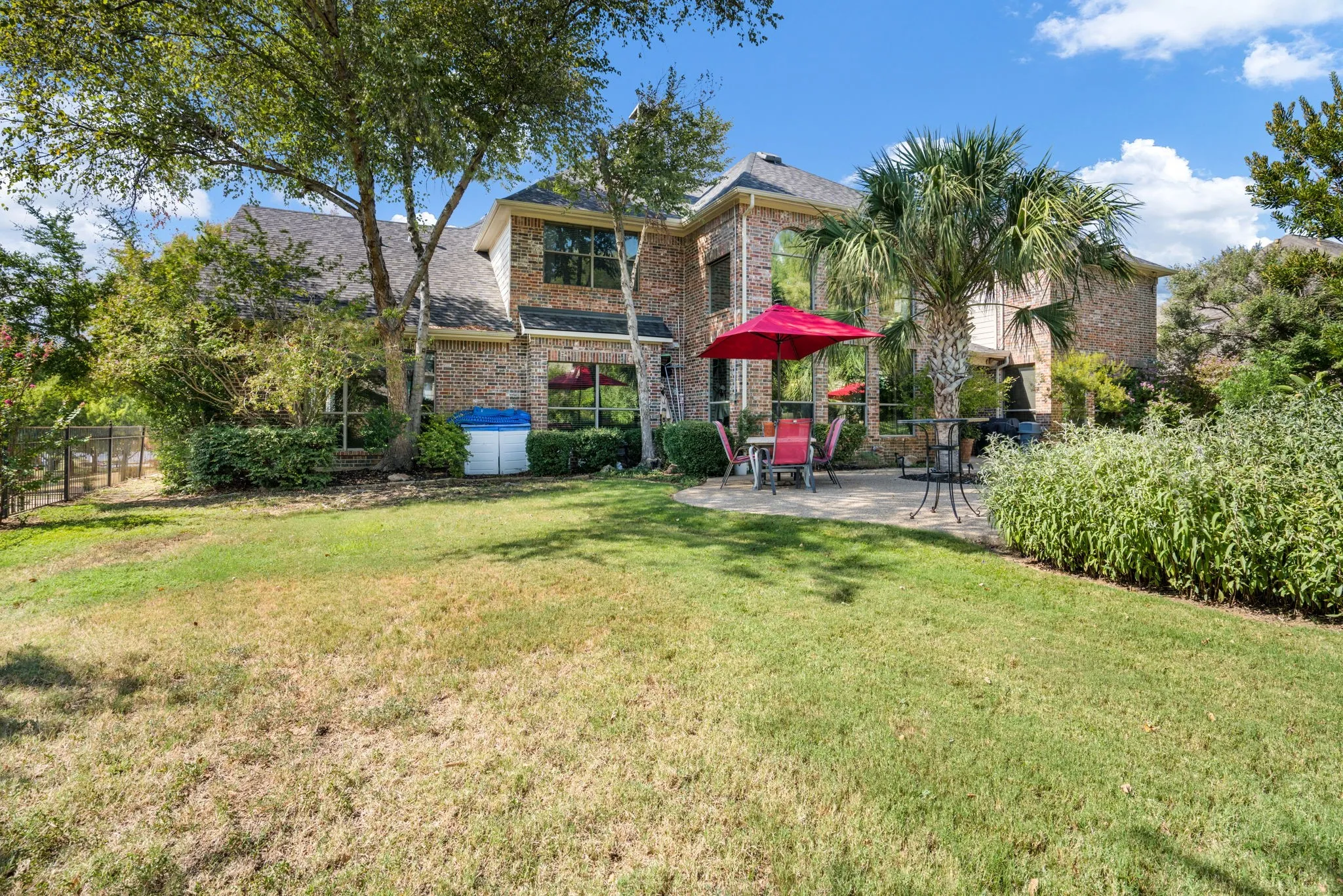 Brick exterior with multiple windows, mature trees, a palm tree, and a paved patio area