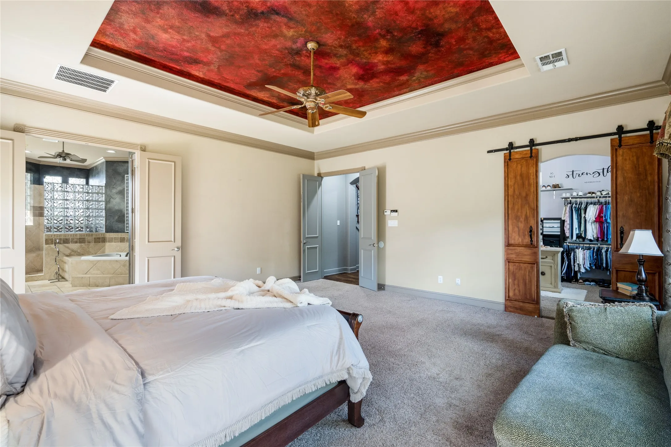 Tray ceiling with decorative finish, ceiling fan, carpet flooring, dual barn doors, and attached bathroom with soaking tub