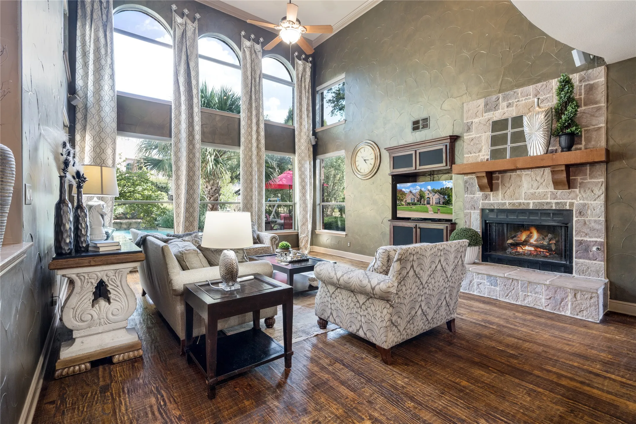 Living area with soaring ceilings, wood-finish flooring, a stone-surround fireplace with a wood mantle, and built-in cabinetry