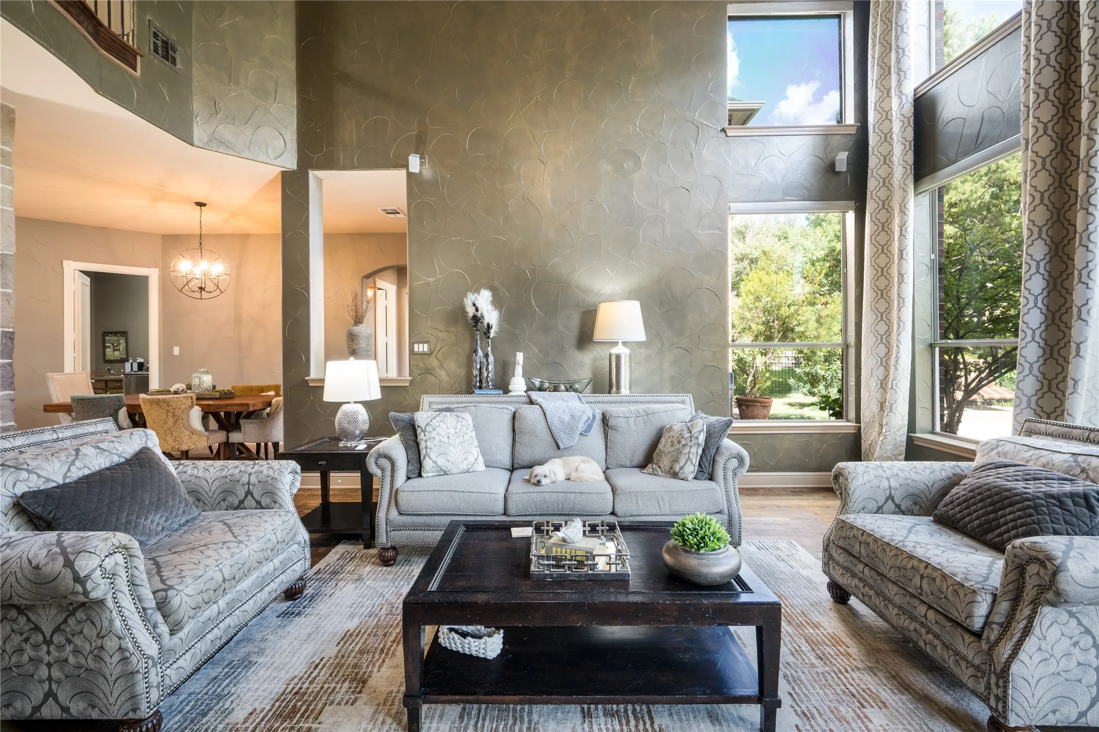 Two-story living area featuring tall windows, textured wall finishes, and a staircase with a wood handrail