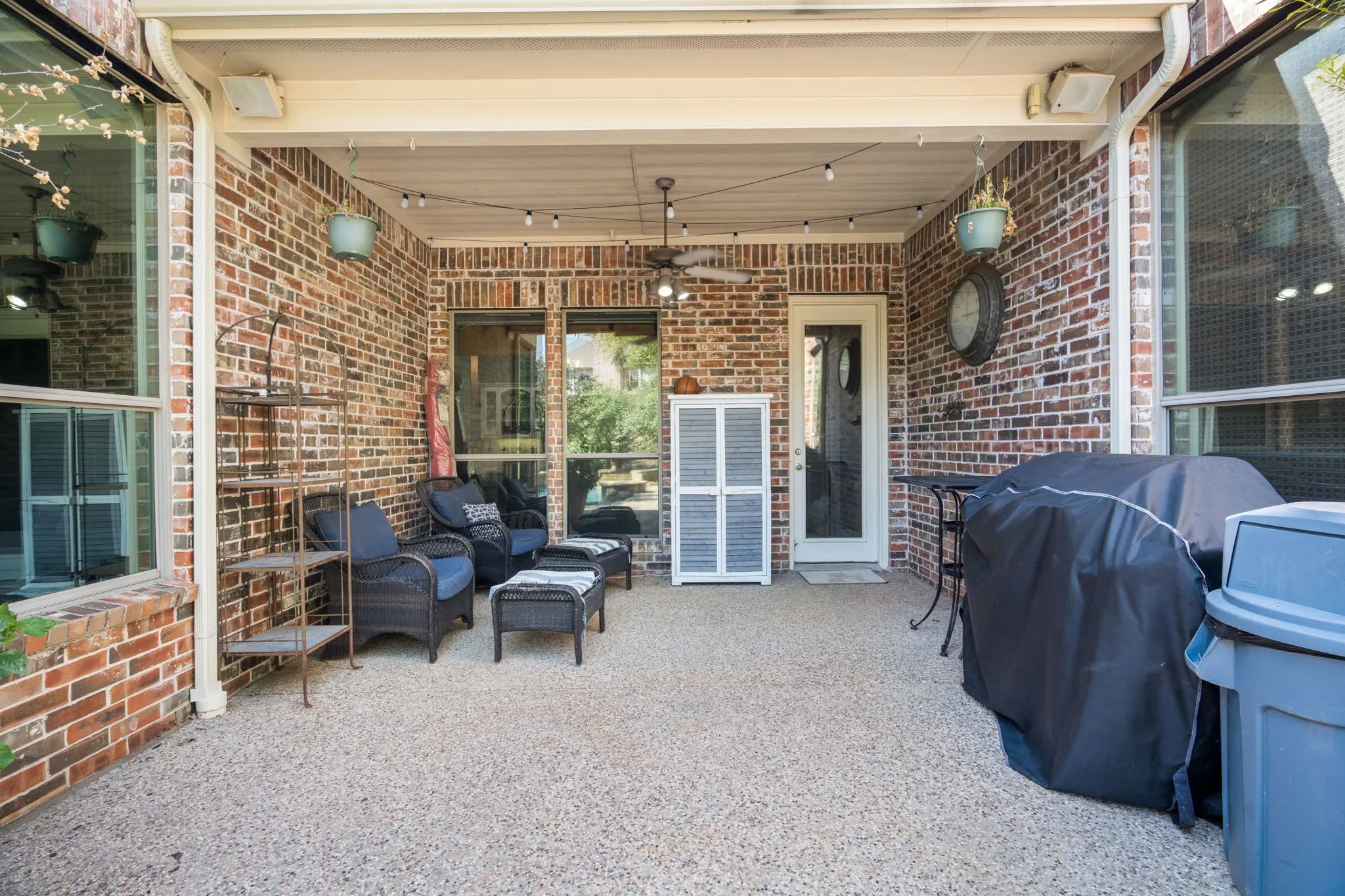 Covered patio featuring a ceiling fan, exposed aggregate flooring, and brick exterior walls