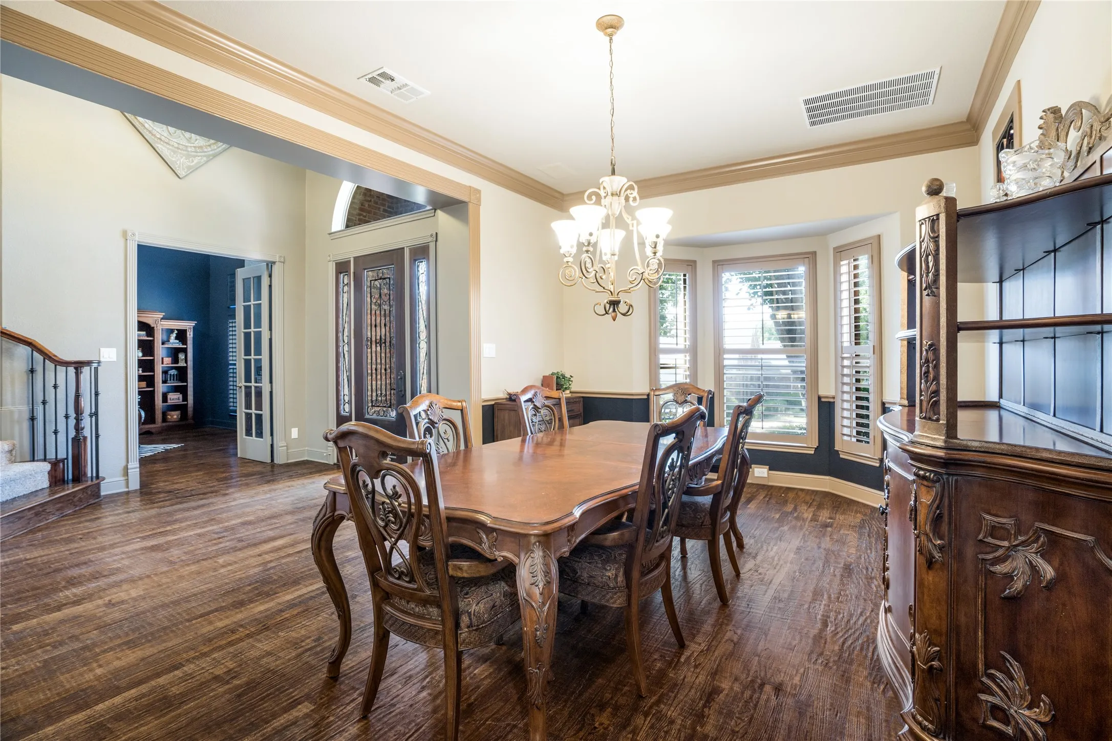 Wood-finish flooring throughout, elegant chandelier, bay window with shutters, and decorative molding